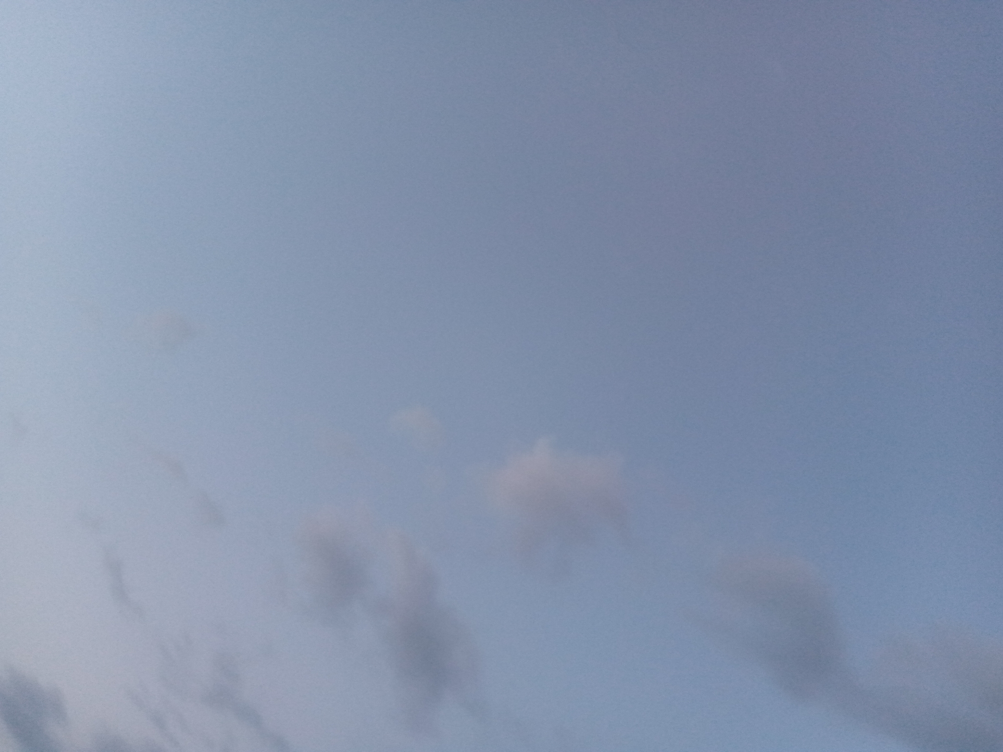 The image displays a pale blue sky with several diffuse, wispy clouds scattered across it. The lighting suggests it might be during twilight or an overcast day. There are no discernible human figures, objects, or structures visible in the frame. The setting appears to be an outdoor environment, with the focus entirely on the sky. No specific location within Serti, Nigeria, can be determined from the visual information provided.
