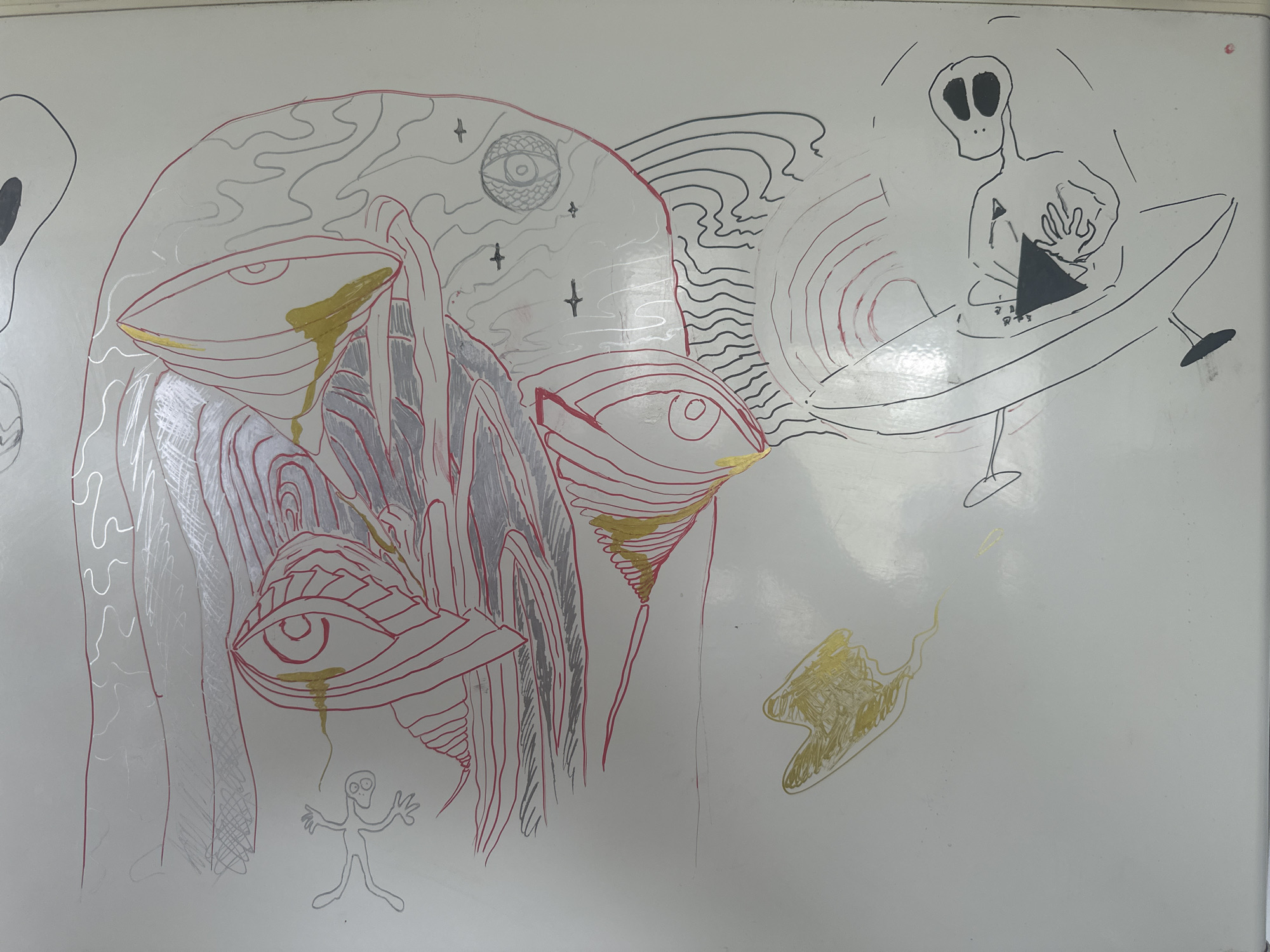 A whiteboard in an unknown location contains a series of drawings in black, red, silver, and gold markers. The drawings include:
* A large, stylized head with multiple eyes, one of which is weeping gold tears. The head also contains star-like markings and concentric line patterns.
* Two small alien-like figures, one under the large head and another to the left of it.
* An alien figure seated in a flying saucer-like object, manipulating a black triangle.
* Other abstract line patterns and shapes.
There is no evidence in the image that indicates this image is located in the city of Chaikovsky, Russia.