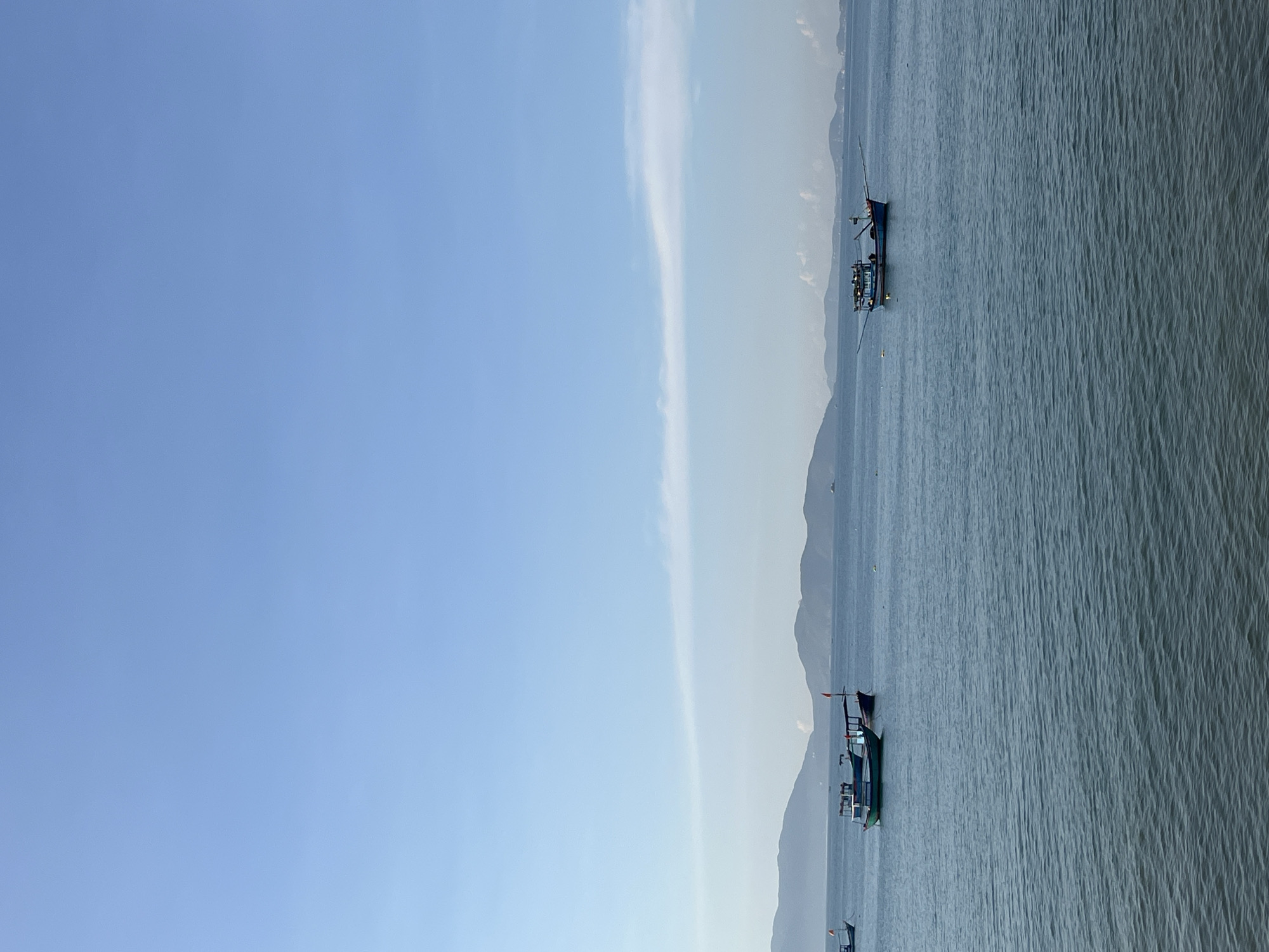 The image shows a seascape scene with several boats on the water. In the background, there are mountains, and a blue sky with some clouds can be seen. The boats appear to be fishing boats. The location is inferred to be in or near Nha Trang City, specifically Bac Nha Trang Ward, Vietnam, based on the inferred mountains and boat types.