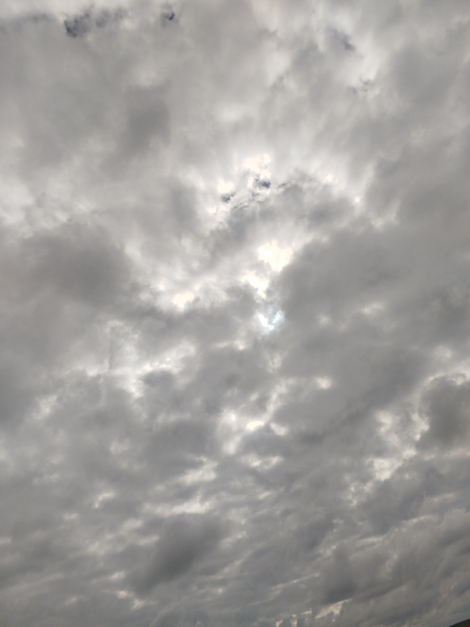 The image shows a cloudy sky with patches of sunlight breaking through. The clouds are varied in thickness and density, with some appearing dark and ominous while others are lighter and more diffused. The overall lighting suggests it is daytime, possibly late afternoon or early evening, given the diffused sunlight. The scene is entirely composed of the sky, with no visible ground, buildings, or people. The location provided, Крывасельскі сельскі Савет, Belarus, indicates an agricultural or rural area, but this is not visually discernible from the image itself.
