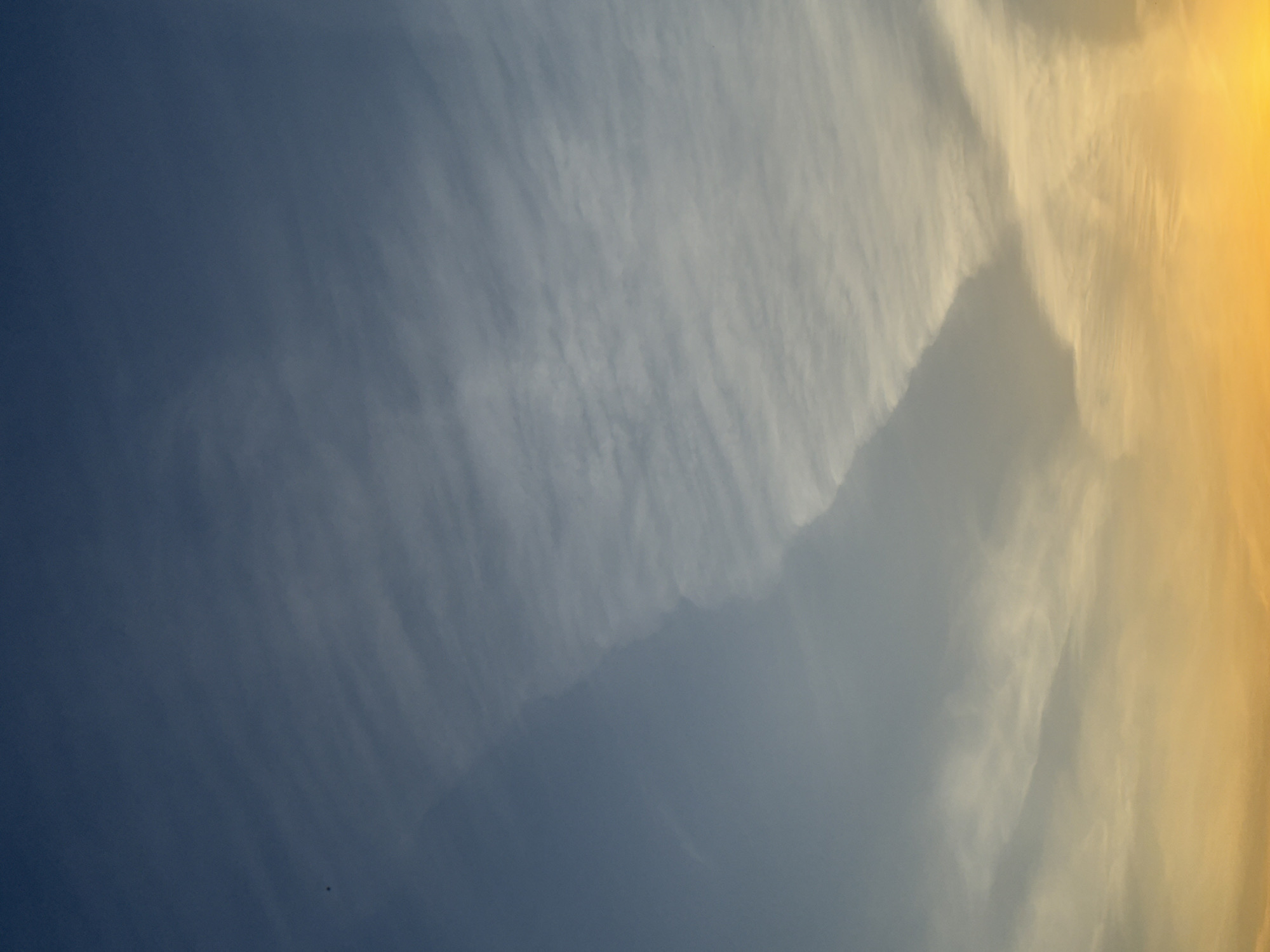 The image shows a sky gradient with a deep blue hue on the left transitioning to a golden yellow on the right. Wispy cirrus clouds are present, primarily concentrated in the middle and right portions of the frame. No specific location or city can be determined from the image.