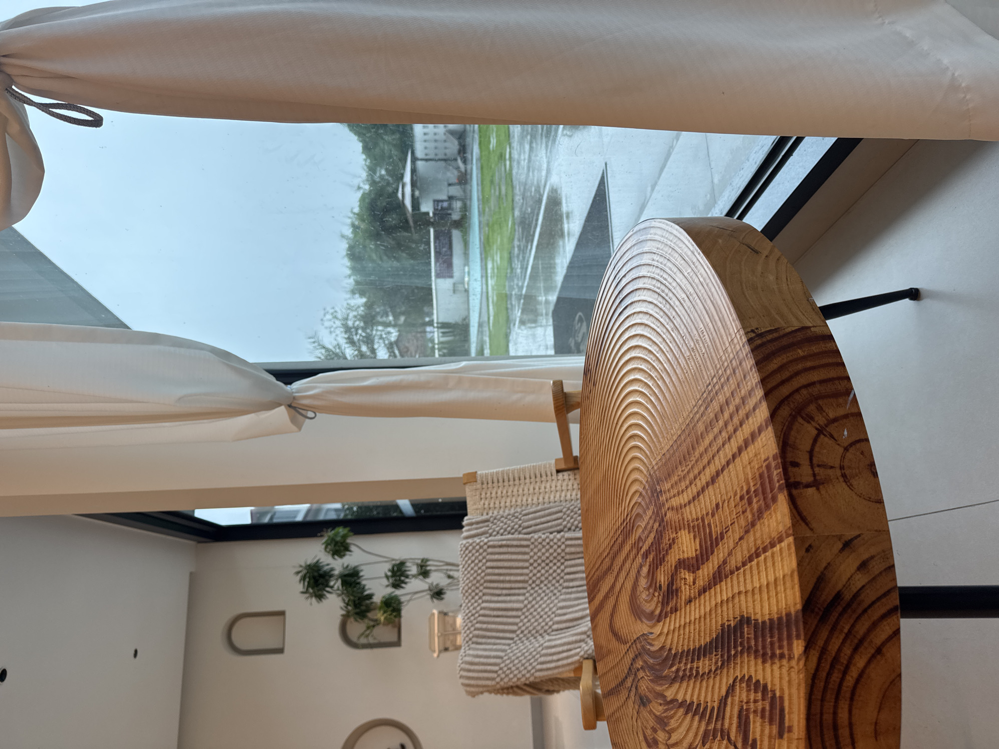 The image presents an interior view with an outdoor scene visible through a window. The interior is characterized by white walls and minimalist decor, featuring arched niches, a potted plant, and what appears to be a wooden decorative piece. The window offers a glimpse of a rainy exterior, with a building across a wet, green landscape. While the image provides some architectural elements, no specific details definitively link it to Guilin, China. If the location is valid it would require additional information.