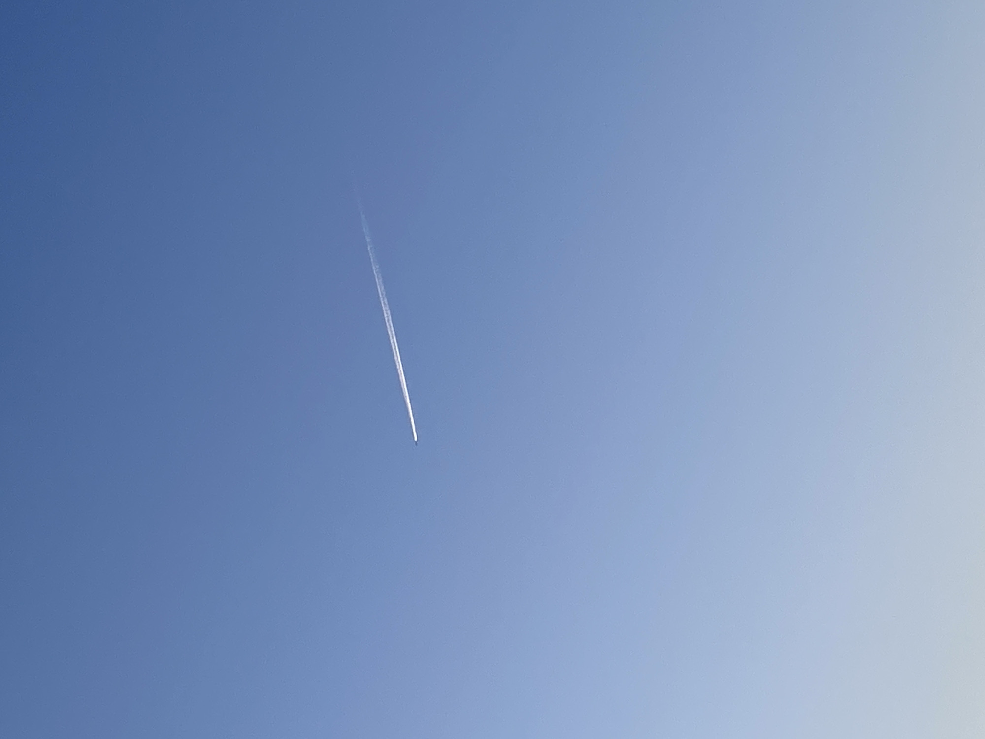 A bright blue sky is seen in the image. A contrail from a high-flying aircraft is visible streaking diagonally across the sky from the center to the upper-left. No other objects or subjects are apparent. The image does not provide enough information to determine if the location is Malyi Bukor, Russia, or to identify any characteristics specific to that city.