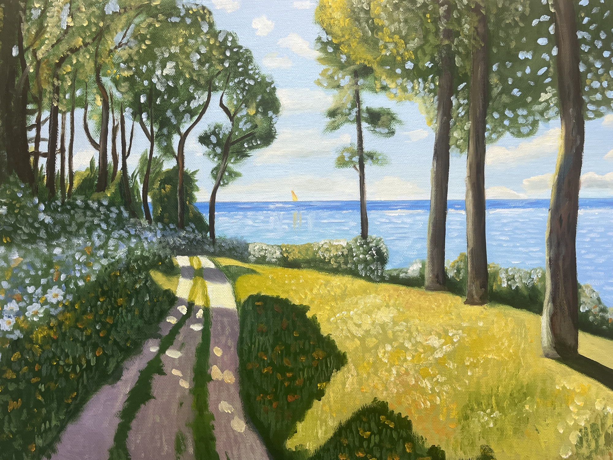 This is a painting of a sun-drenched path leading towards a body of water, likely the sea, with a small sailboat visible in the distance. The path, paved with gravel, is dappled with sunlight and shadows, creating a textured and inviting foreground. Lush green trees with clusters of white and yellow blossoms line the path on the left, while a grassy field dotted with wildflowers stretches out to the right. Several tall trees with dark trunks are positioned on the right side of the composition, framing the view of the water. The water itself is a vibrant blue, reflecting the clear sky above, which is dotted with white, fluffy clouds. The overall impression is one of a peaceful, idyllic coastal landscape.