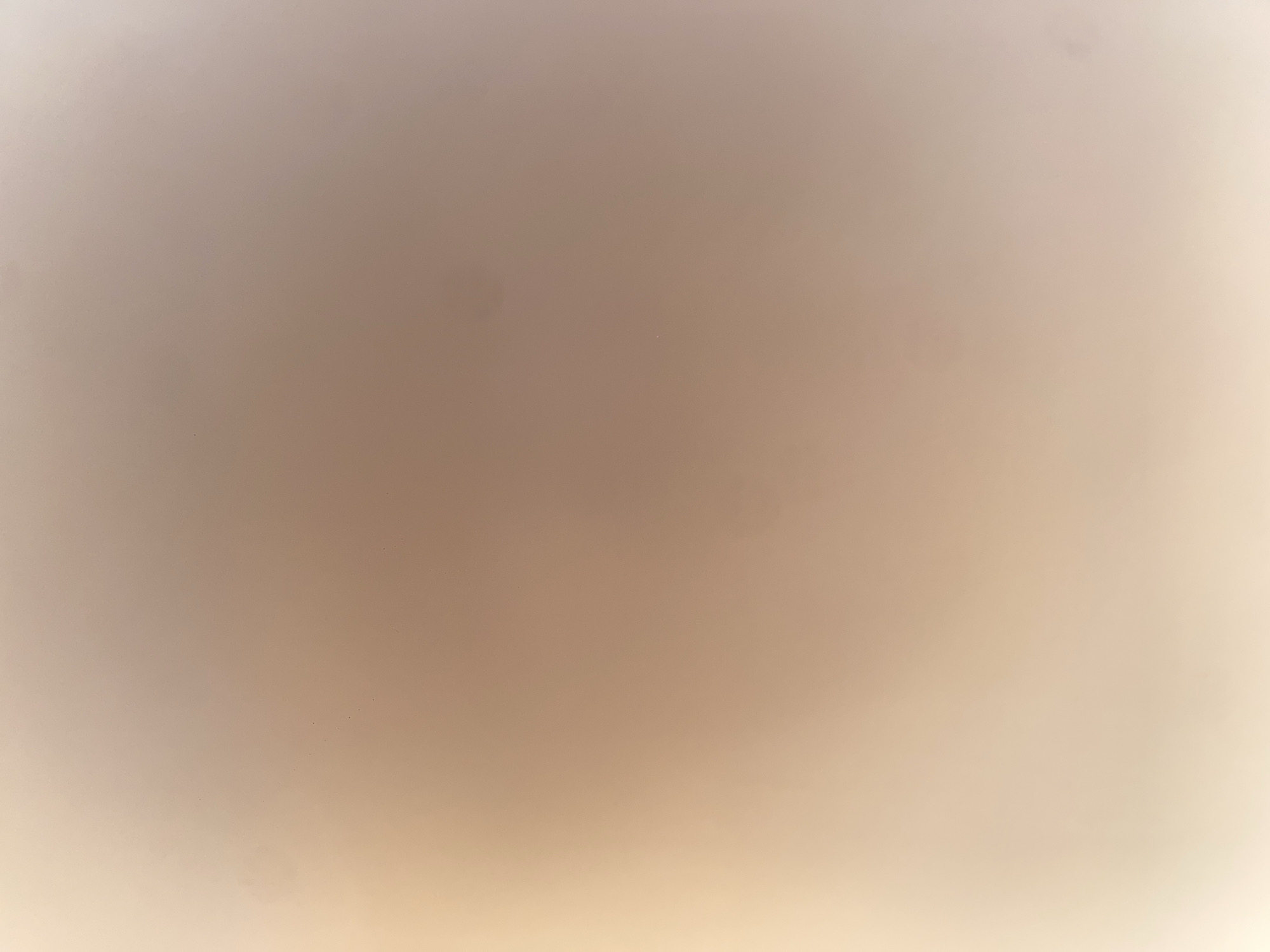 The image displays a blurred, gradient background with subtle variations in color, ranging from a pale beige on the left to a light pinkish-brown on the right. There are a few small, dark specks scattered throughout the image, possibly dust or imperfections. The lighting appears to be soft and diffused, creating a hazy effect. There are no discernible people, subjects, objects, actions, or interactions visible in the image, nor any contextual clues that would suggest its location in the city of Ablanitsa, Bulgaria, or any other specific geographic setting. The overall impression is that of an abstract or out-of-focus photograph.