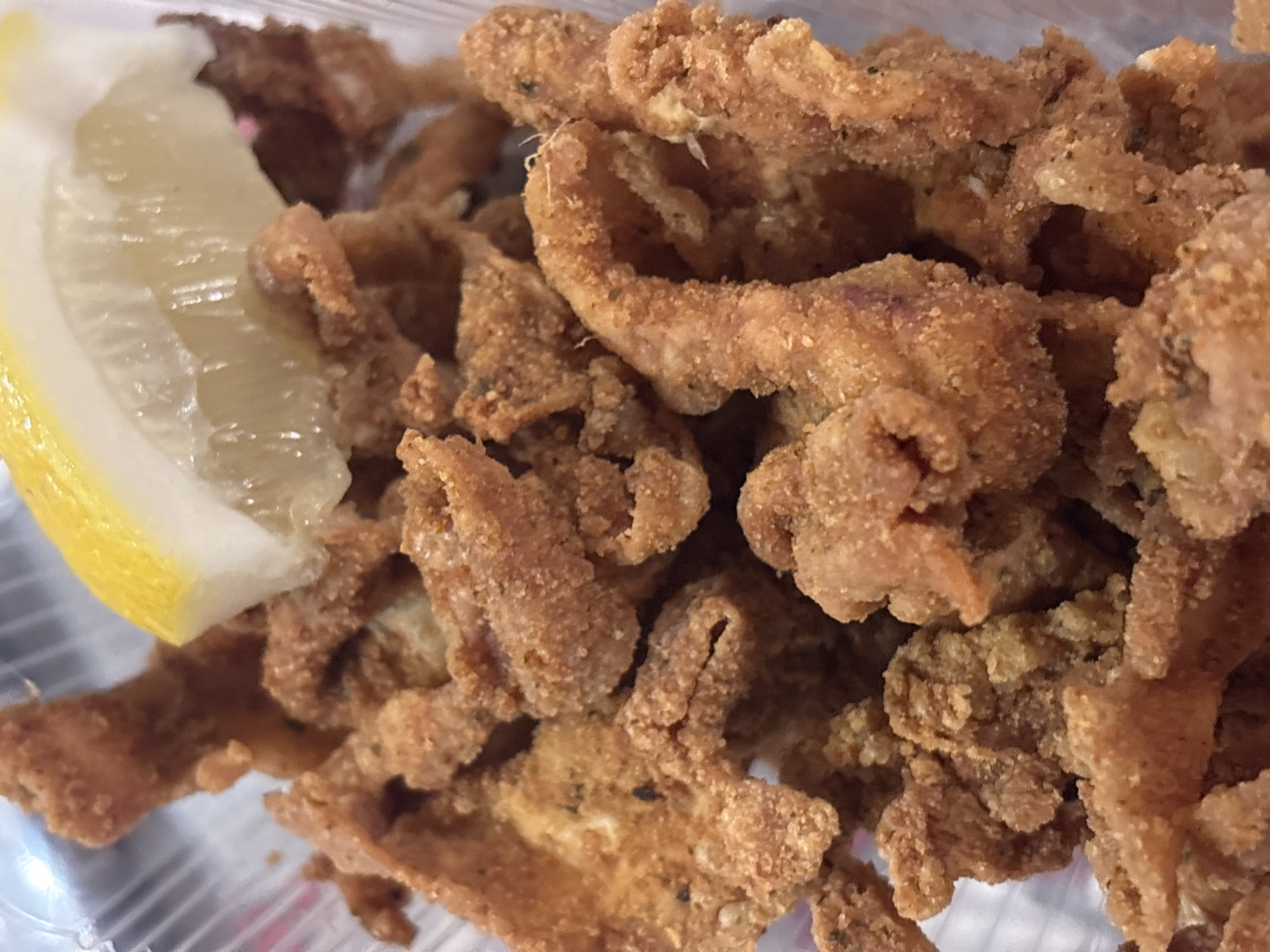 A close-up shot reveals a portion of fried chicken gizzards served with a lemon wedge, likely in a plastic container. The gizzards are coated in a crispy, golden-brown batter, and some appear curled or twisted. The lemon wedge has a yellow rind and translucent flesh. The location within Sofia, Bulgaria, cannot be determined from the image.