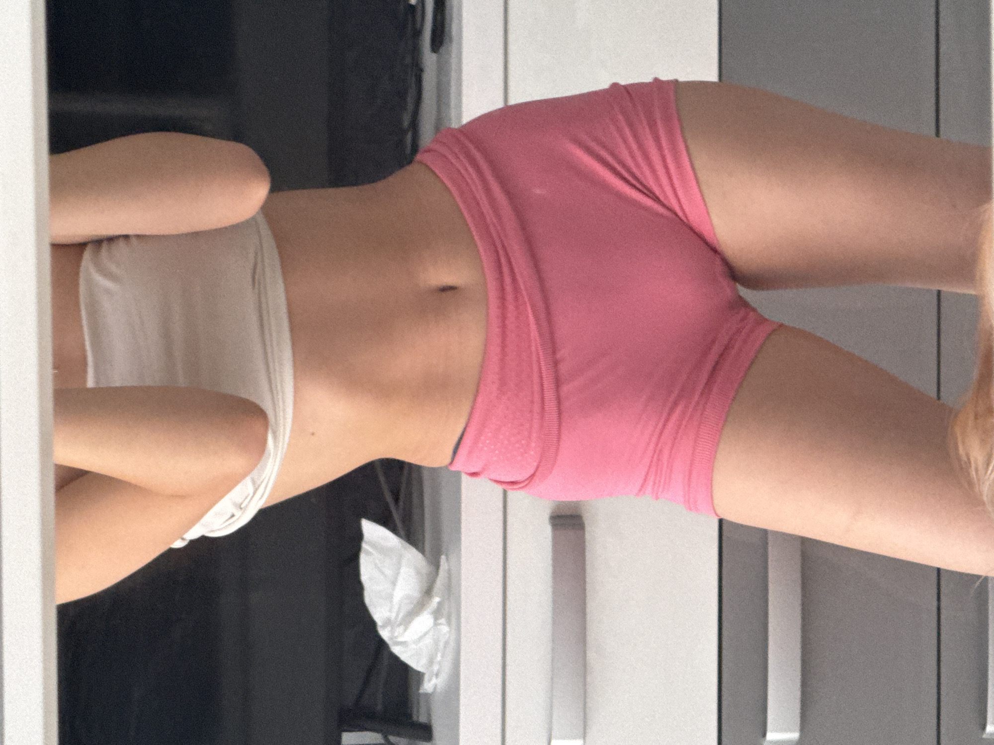 The image shows a close-up, waist-down view of a person wearing a white strapless top and pink shorts. The person's skin tone is fair. They are standing in what appears to be a bedroom. In the background, a white dresser with silver handles is visible, as well as a dark surface, possibly a television or a piece of furniture. A crumpled white tissue is on the dresser to the left. The lighting suggests an indoor setting. The image does not contain information about the city of Sofia, Bulgaria.
