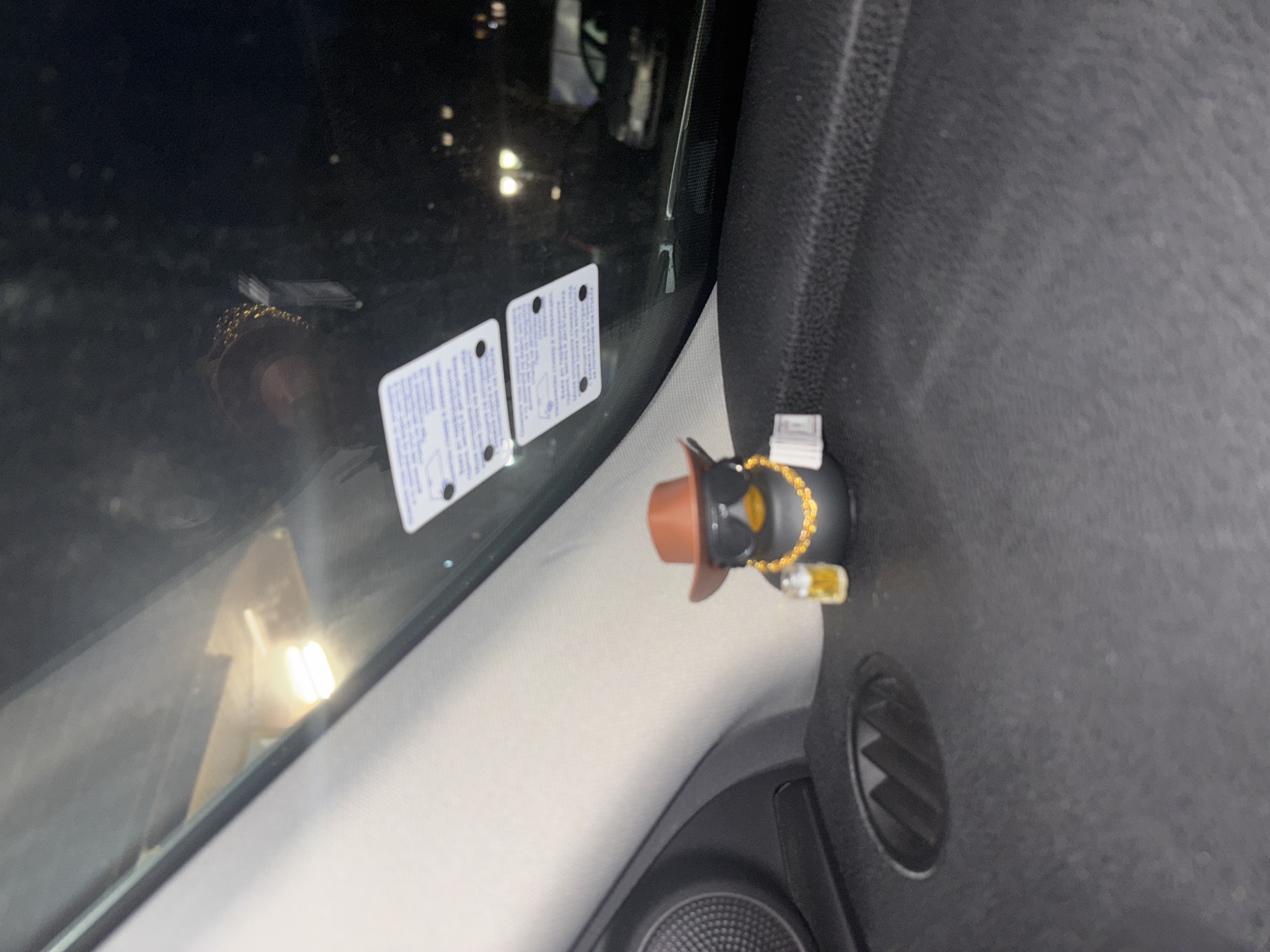 The image shows the interior of a car, with a bobblehead doll wearing a cowboy hat and sunglasses, positioned on the dashboard next to an air vent. Two stickers are adhered to the windshield. The scene does not provide sufficient information to determine its location in Zlatograd, Bulgaria.