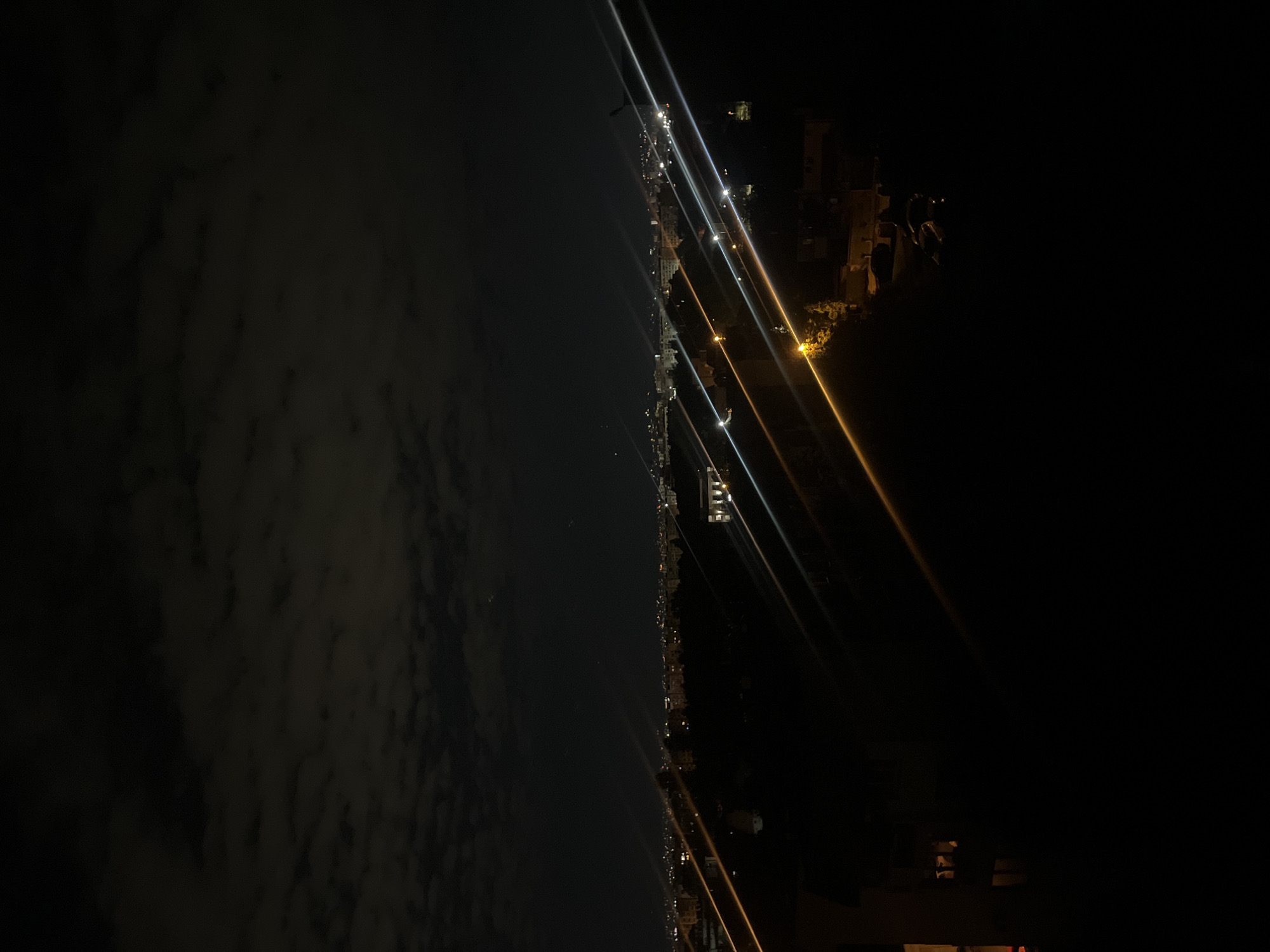 This is a nighttime image taken from what appears to be an elevated position in Sofia, Bulgaria. The horizon is divided between cloudy dark sky on the left and city lights on the right, including lights on a cable car system. Streetlights and building lights illuminate areas of the city below. The location is probably somewhere along the Vitosha Mountain, considering the aerial ropeways.