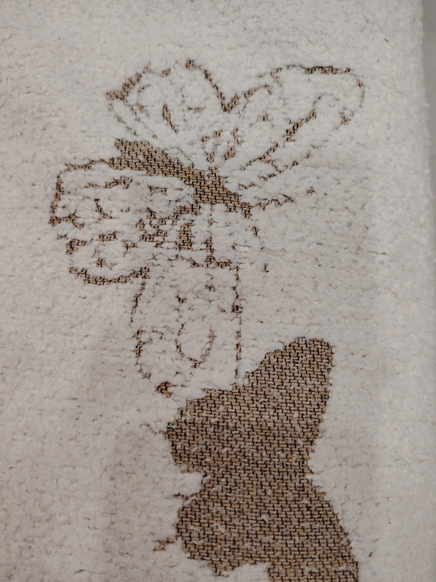 A close-up shot shows a flower-shaped design woven into a carpet or rug. The flower appears to have multiple petals and a stem. The carpet is textured with looped fibers. The flower design is darker than the carpet's background. No people, actions, interactions, or specific environmental details suggesting a location are apparent. The location of Sarapul, Russia, is not discernible from the image.