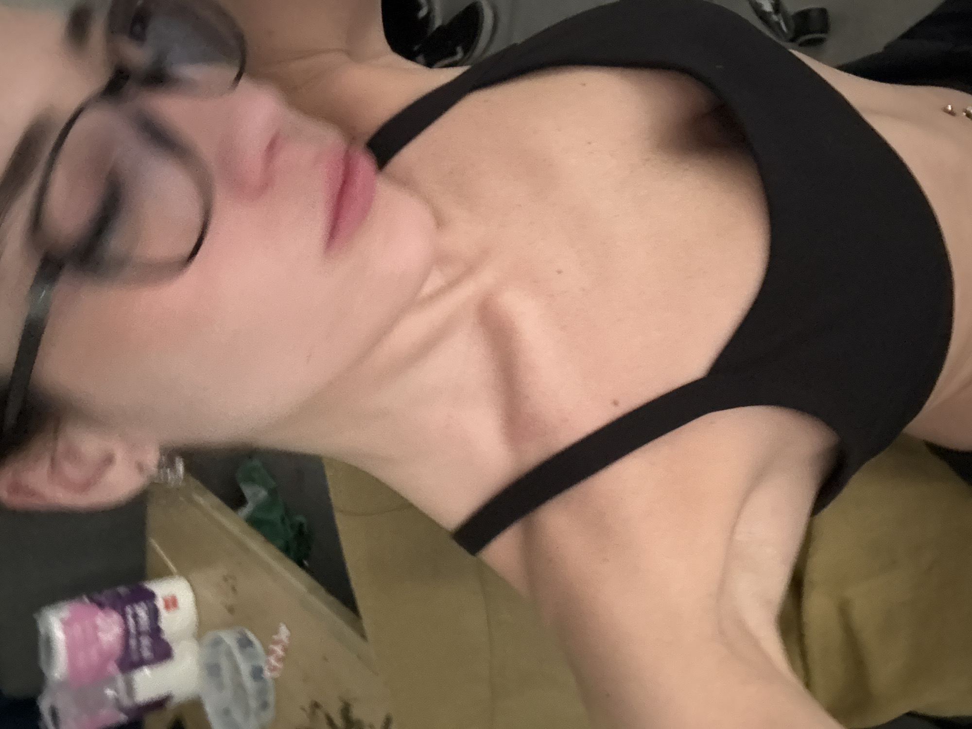 A woman wearing glasses and a black sports bra is lying down. The image is taken at an unusual angle. The location is unclear, but objects next to her could be on a nightstand, including some toiletries. There is no evidence of the city of Buenos Aires, Argentina.