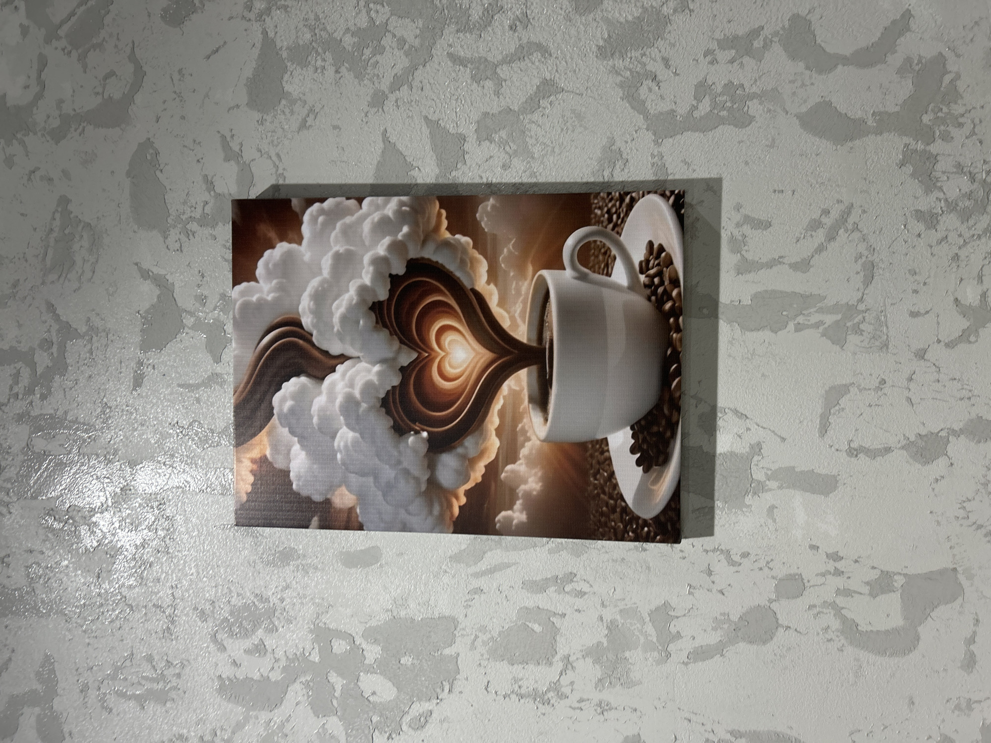 A canvas print featuring a coffee cup with a heart-shaped latte art design is hanging on a textured, light gray wall. The print depicts a white mug filled with dark coffee, surrounded by coffee beans on a white saucer. Above the mug, clouds are swirling, and the steam from the coffee is forming a heart shape with intricate layers. The background of the print shows a sunrise or sunset with a warm orange glow and silhouetted clouds. The wall has a rough, uneven texture with variations in shade, suggesting a plaster or stucco finish. The image is taken from a straight-on, slightly angled perspective. This scene is not specifically located in the city of Chaikovsky, Russia; it is a general interior scene.