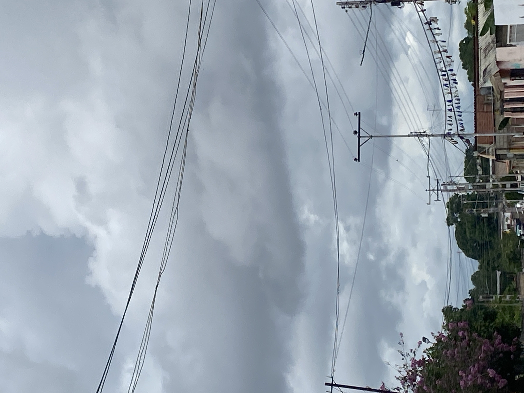 The image depicts an overcast sky with power lines dominating the upper portion of the frame. In the distance, buildings are visible with some greenery. The location is identified as Tinaquillo, Venezuela. No people are visible in the image.