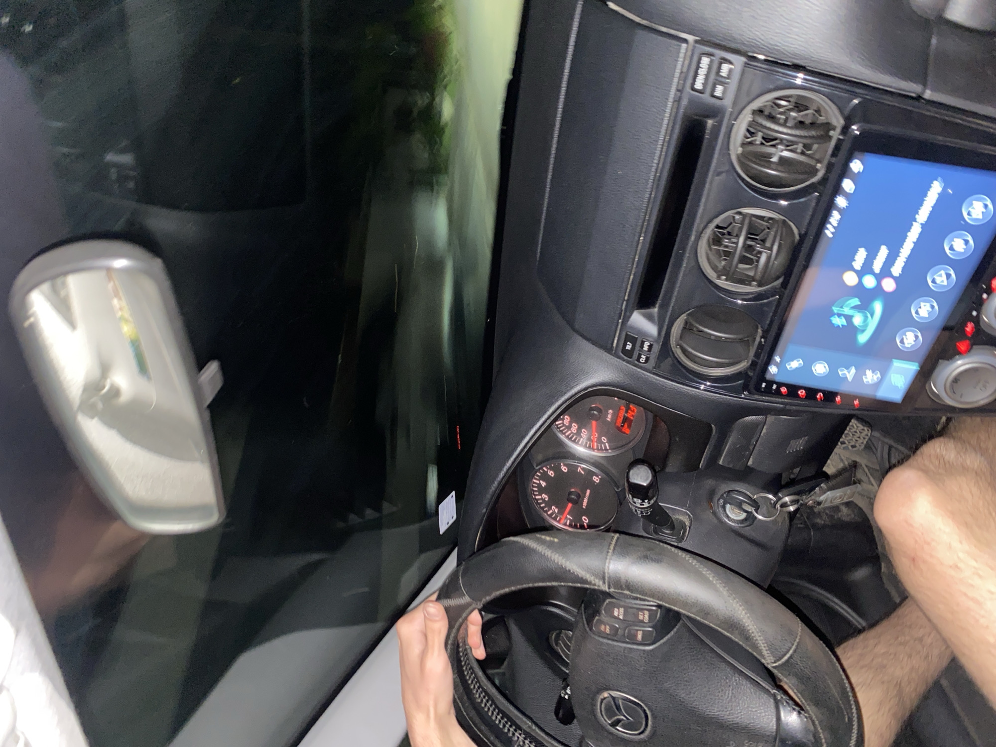 The image shows the interior of a car, looking forward through the windshield at night. The driver's hand is on the steering wheel, and the dashboard is visible with instruments like the speedometer and tachometer. A digital display is also present in the center console. The scene is dark outside the car, with streetlights or headlights illuminating a road. There is no visible indication of the specific location within the city of Yasen, Bulgaria.