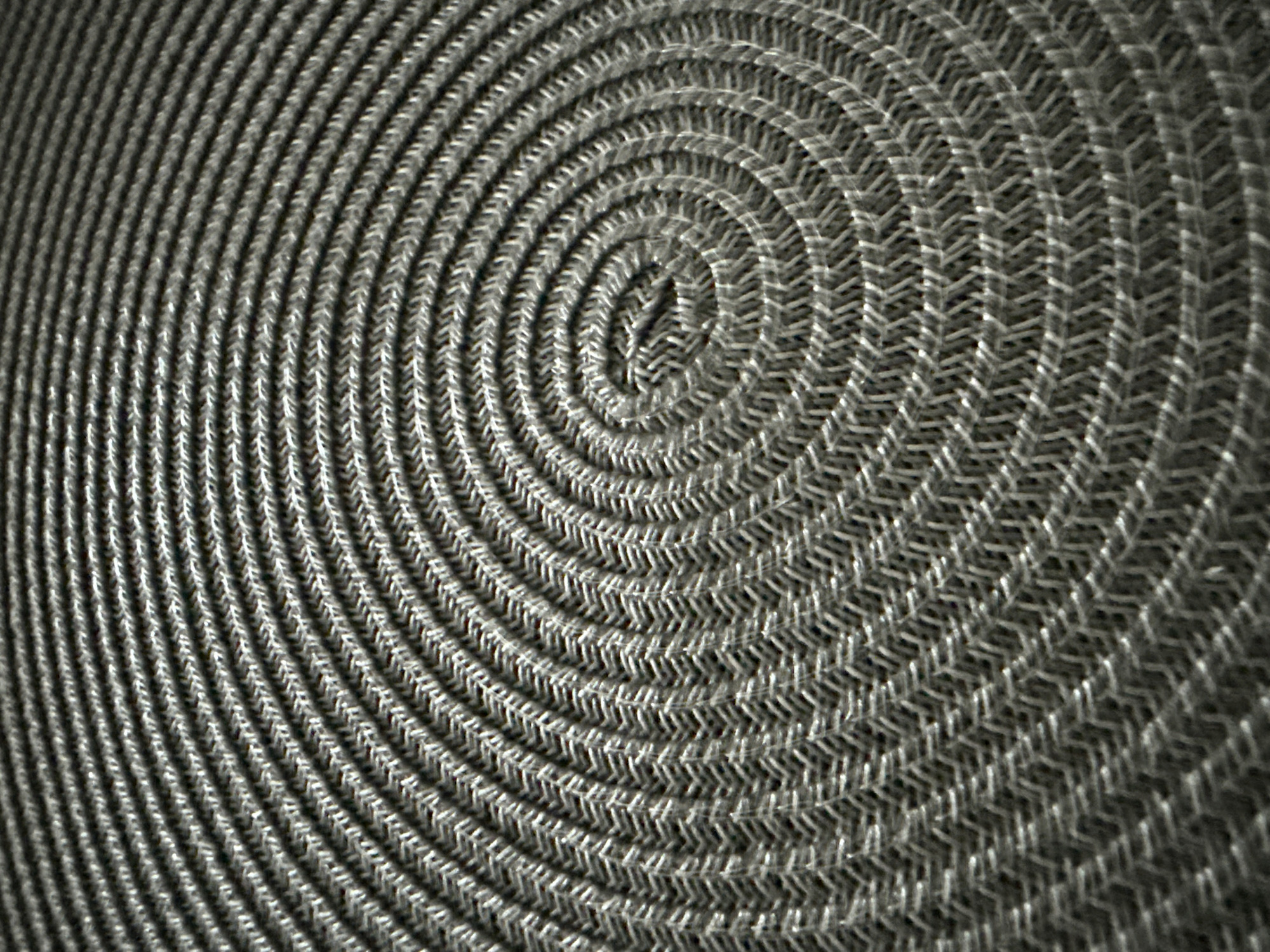 This media file is a close-up, abstract shot of a coiled, woven material, likely a metal mesh or a similar textured fabric. The coiling creates a spiral pattern that begins tightly in the center and expands outwards. The texture is characterized by a repeating, interlocking design, resembling small "V" shapes or chevrons. The lighting creates highlights and shadows that emphasize the three-dimensional quality of the weave. There is no discernible text, people, or specific scene. The focus is entirely on the intricate pattern and texture of the coiled object. The context of Vinnytsia, Ukraine, does not offer any direct visual cues within the image itself, as it is an abstract composition.