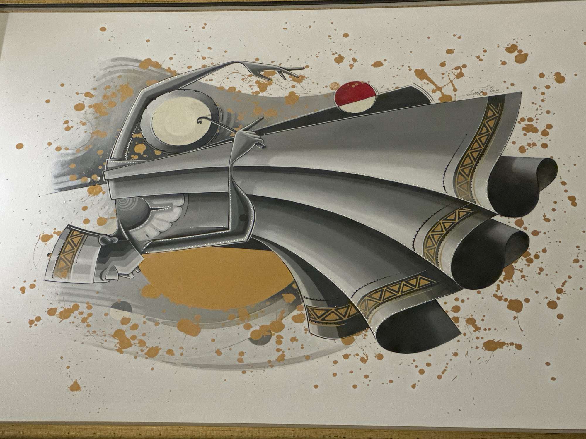 A framed abstract artwork depicts a grey, quasi-mechanical figure playing a drum. The figure is angular, with geometric shapes suggesting clothing and limbs. The hands hold drumsticks. The drum itself is a circular shape with a white surface. A red and white disc floats above the figure's head. The artwork is set against a white background with gold and grey splatter patterns. The work is signed in the upper right corner. This image is a representation of art, not a location in the city of Ilado, Nigeria.