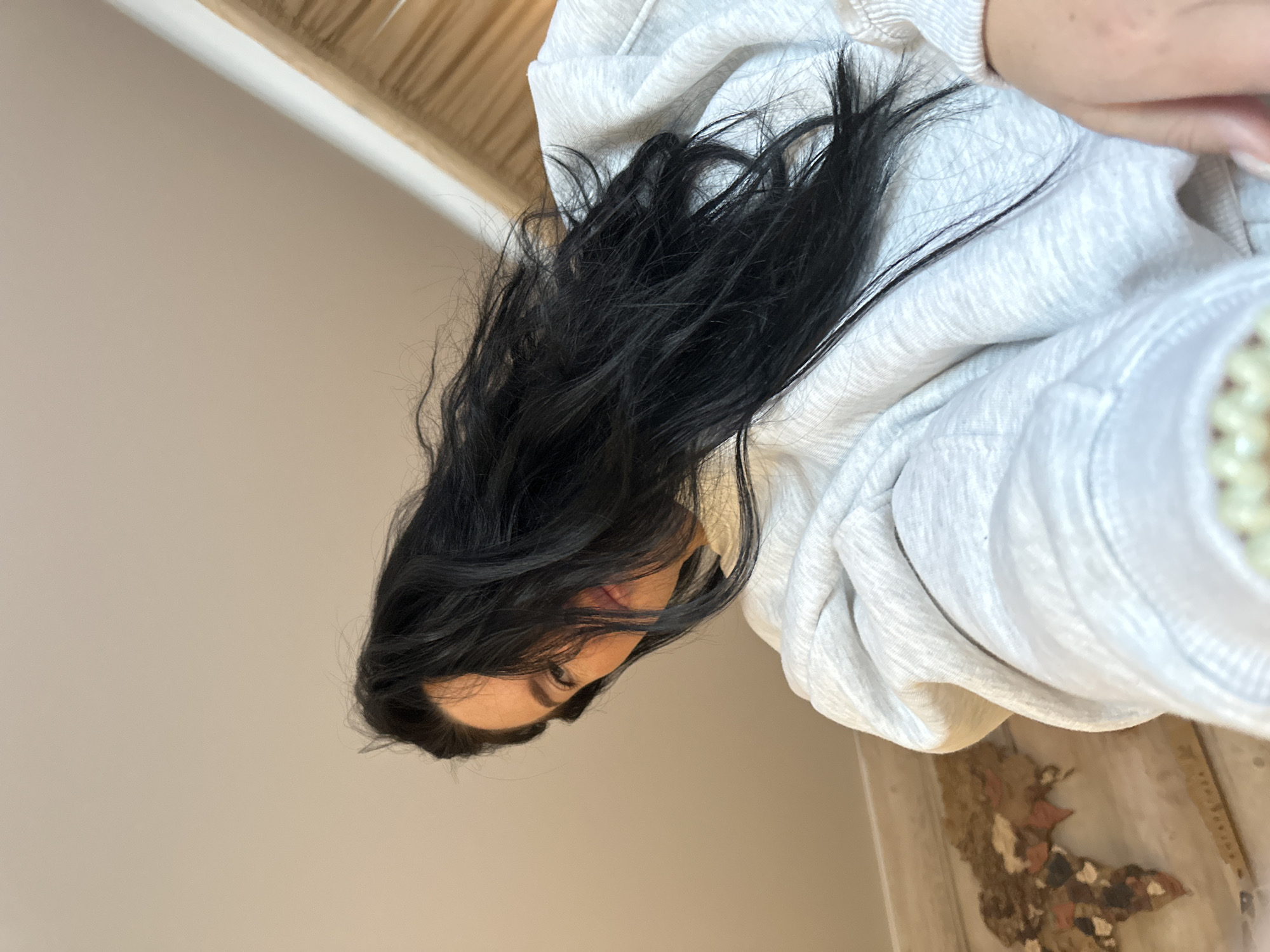 A woman with long, dark hair is wearing a light gray hooded sweatshirt. She is indoors, near a ceiling with light wood trim and a wall. The floor appears to be light-colored and decorated with tiles or a design. Location: Ольховка, Russia not discernible from the image.