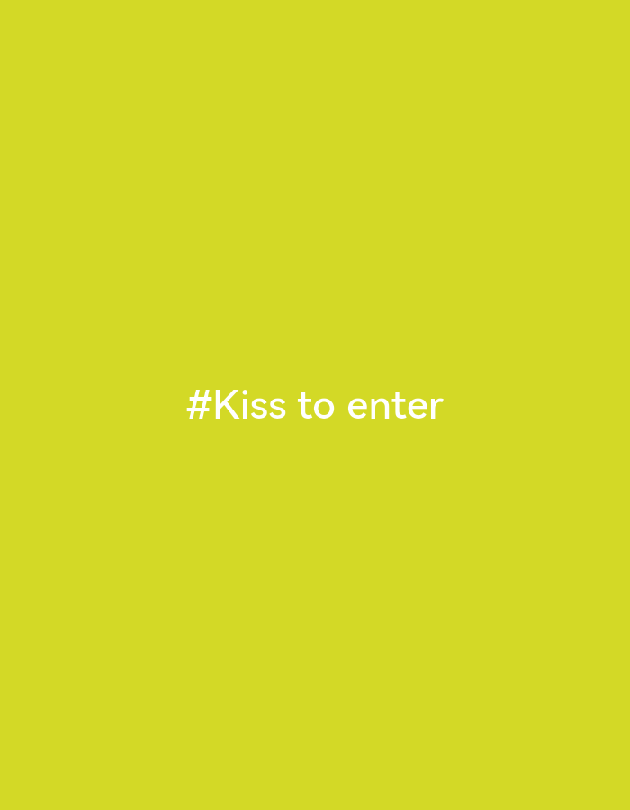 The image displays white text "#Kiss to enter" centered on a solid, vibrant chartreuse-yellow background. There are no other subjects, objects, or discernible scene elements. No specific activity or event is depicted, nor are there any cues for time of day, weather, or location. The overall impression is minimalist, focusing solely on the text against the bright color.