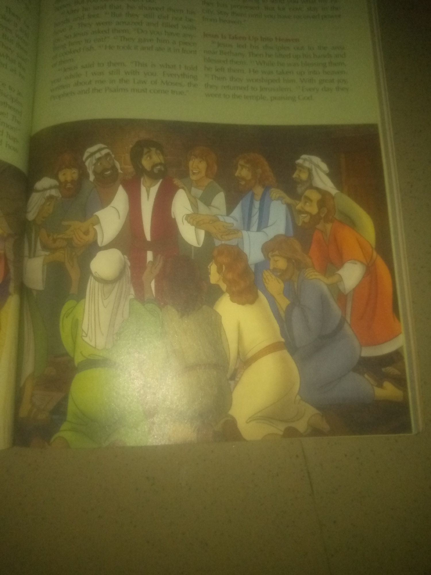 The image depicts an illustration from a religious text, likely the Bible, showing Jesus with a group of disciples. Jesus, in the center with a red garment, is interacting with his followers. Some disciples are looking at him, while others are reaching out or praying. The scene is set indoors, possibly a room where a meal is taking place, as suggested by the presence of food items on a table in the foreground. The overall atmosphere appears to be one of reverence and fellowship.
There is no visual information in the image to suggest a location in Jauro Yinu, Nigeria.