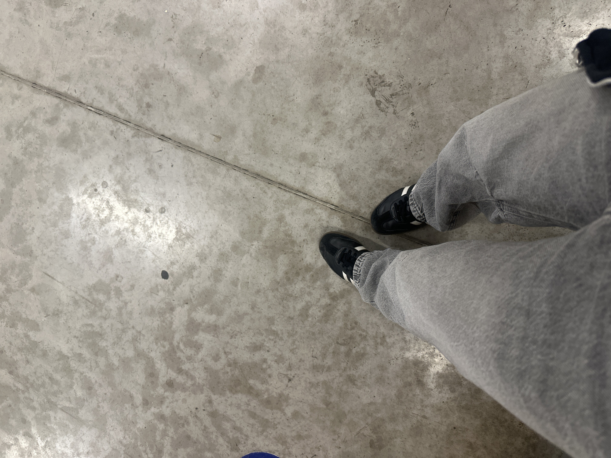 The image depicts a person standing on a concrete floor, likely indoors. The person is wearing grey jeans and black sneakers with white stripes. A thin, dark line runs across the concrete floor. The context of the location being in Mexico City, Mexico, cannot be verified from the image alone.