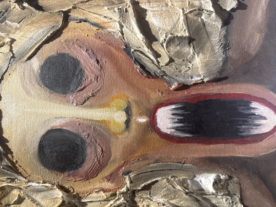 A close-up of an abstract oil painting. Two large, black, round eyes dominate the scene, rendered with thick, textured paint. A small, yellow, bone-shaped nose sits between the eyes. To the right, a large, open mouth with a red outline reveals a dark interior with white horizontal strokes. The surrounding skin tones are various shades of brown and beige. The painting features a heavy, textured surface with visible brushstrokes.