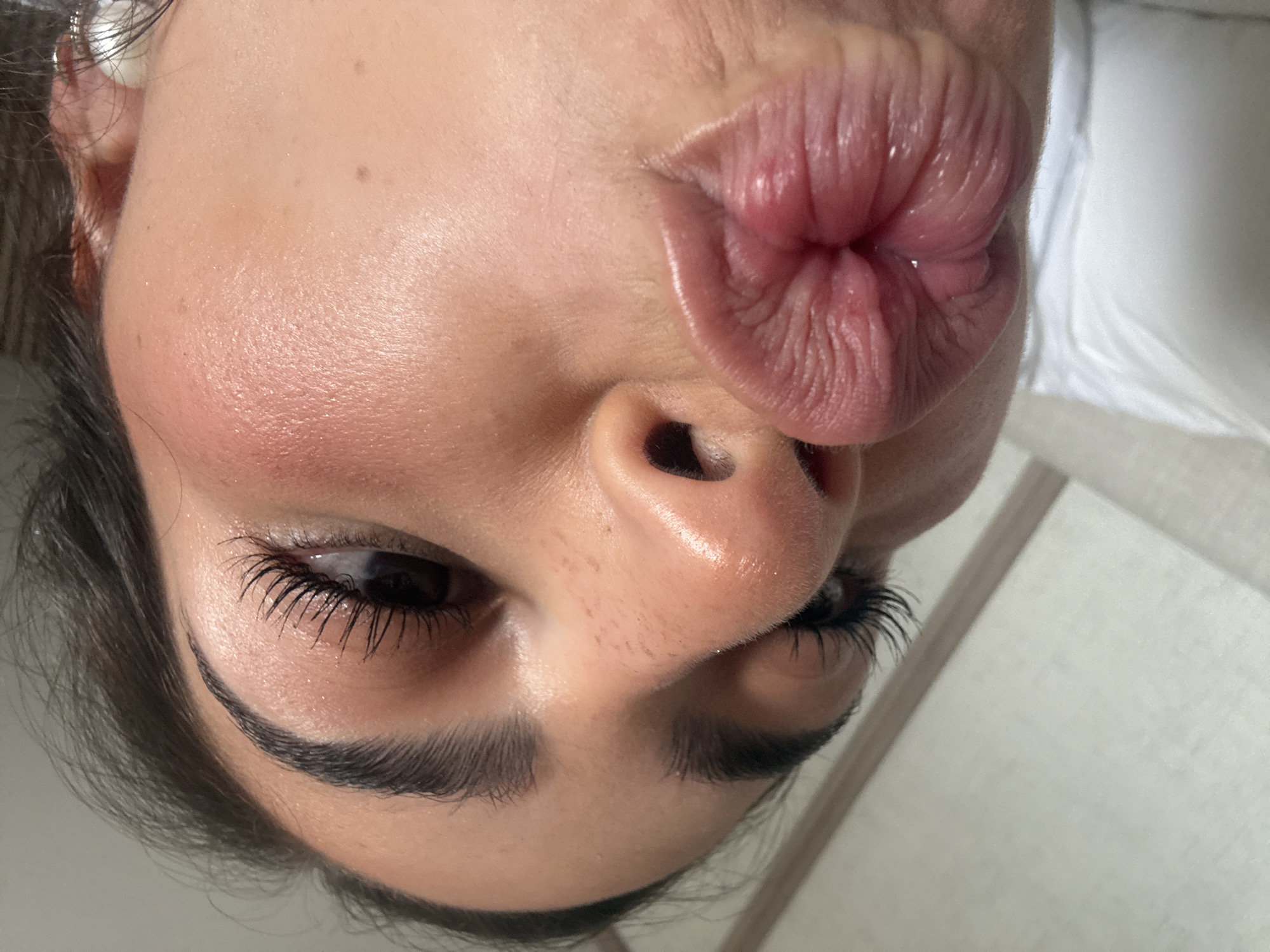 A close-up, rotated image shows a person's face with pursed lips, positioned above the nose. The person has dark eyes and eyebrows with visible eyelashes. Skin texture is evident, including pores and fine lines. The background is out of focus and provides no clues as to a location in San Bernardino Tlaxcalancingo, Mexico or any other specific place. There are no other identifiable objects, actions, or interactions.