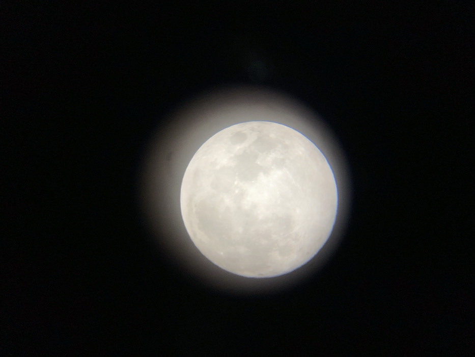 A brightly illuminated full moon is depicted centered against a dark, clear night sky, observed from Buenos Aires, Argentina. The spherical lunar disk shows detailed surface features, including variations in albedo indicative of maria and numerous crater formations. A subtle circular vignetting effect surrounds the moon, suggesting the image was captured through an optical instrument. There are no people, other celestial bodies, artificial objects, actions, or interactions visible within the scene.