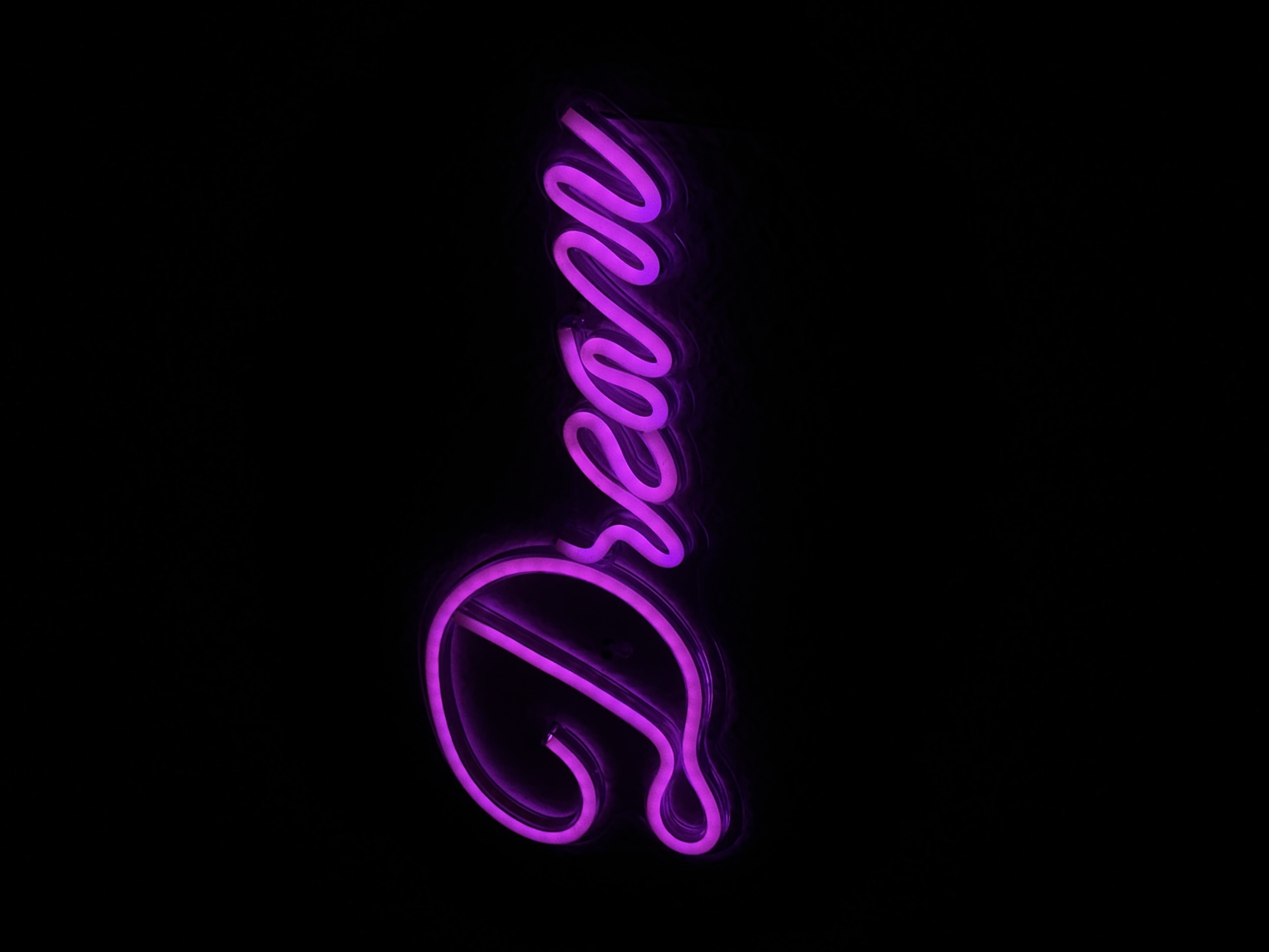 The image shows the word "Dream" spelled out vertically in purple neon lights against a black background. There is no discernible information to suggest the location of San Bernardino Tlaxcalancingo, Mexico. There are no people, subjects, objects, actions or interactions aside from the word "Dream." The environment is a dark void.