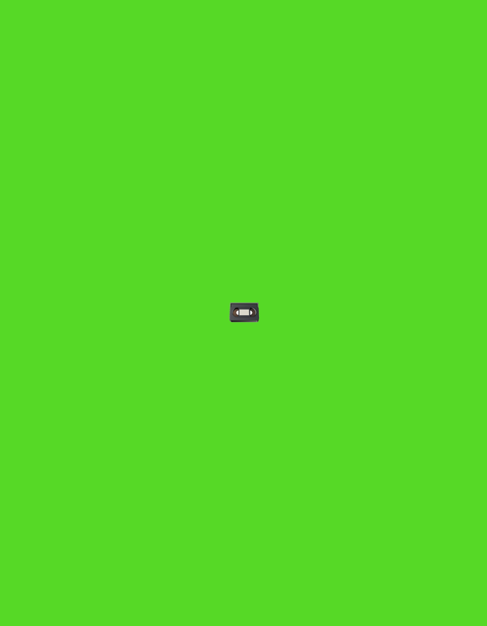 The media file is a close-up, centered shot of a VHS tape against a vibrant green background. The VHS tape is dark gray or black with a lighter gray or white label area and a small, visible spool or mechanism on its left side. The tape appears to be a standard size, possibly for video recording or playback. There are no people, animals, or any other objects visible in the frame besides the VHS tape. The background is a solid, uniform bright green, suggesting a studio or chroma key environment. There is no discernible text on the VHS tape itself. The lighting is even and appears to be artificial, casting no strong shadows. The overall impression is that of a product shot or an isolated object presentation. The setting is not identifiable beyond the green screen, and no environmental cues like time of day or weather are present. The activity or event is not discernible; the tape is static and presented in isolation.