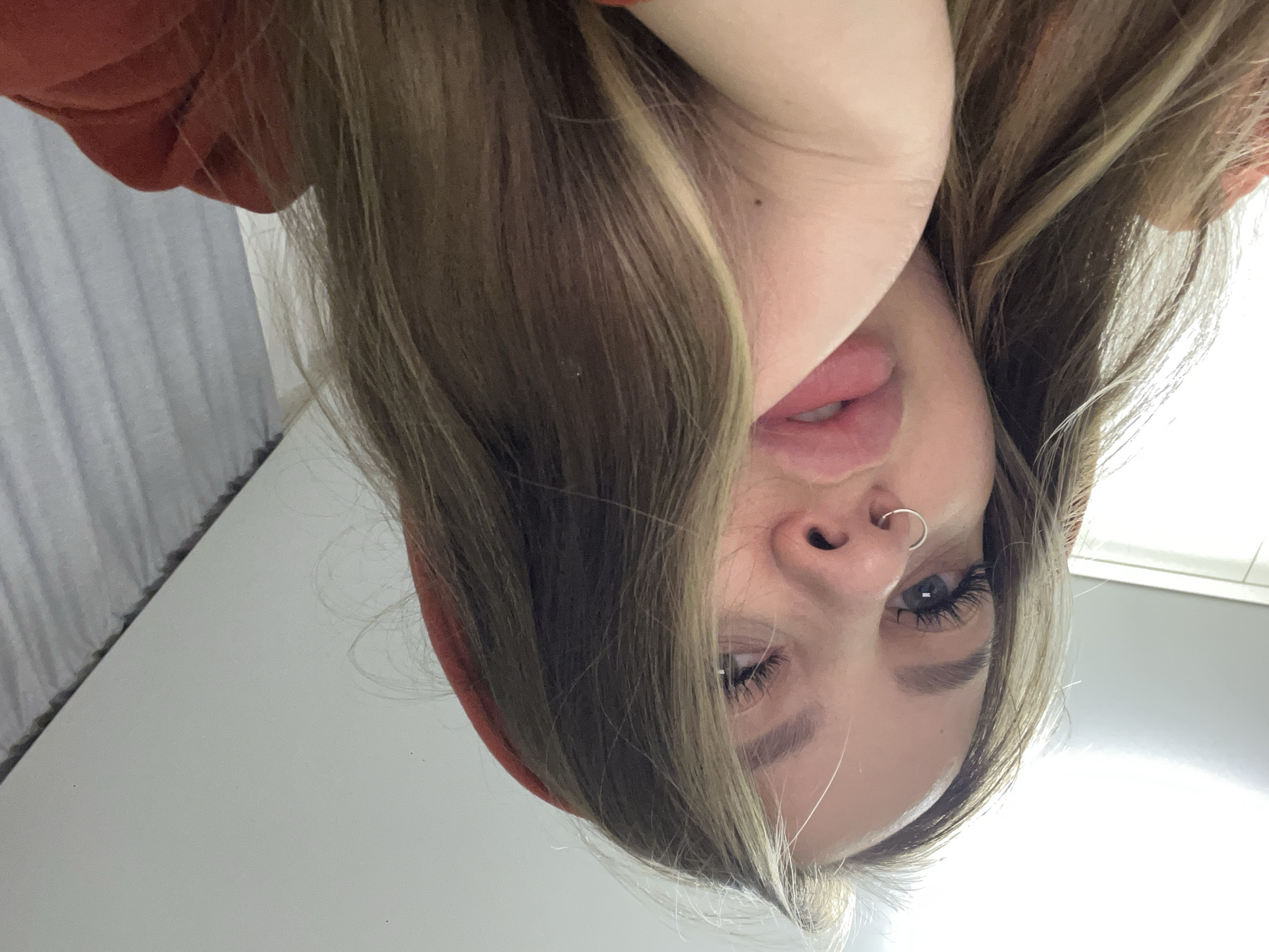 A selfie of a woman with blonde hair, wearing an orange hoodie. She has a nose ring and appears to be tilting her head toward the camera. The background is a plain wall. There is no information in the image indicating that it was taken in Krasnodar, Russia.