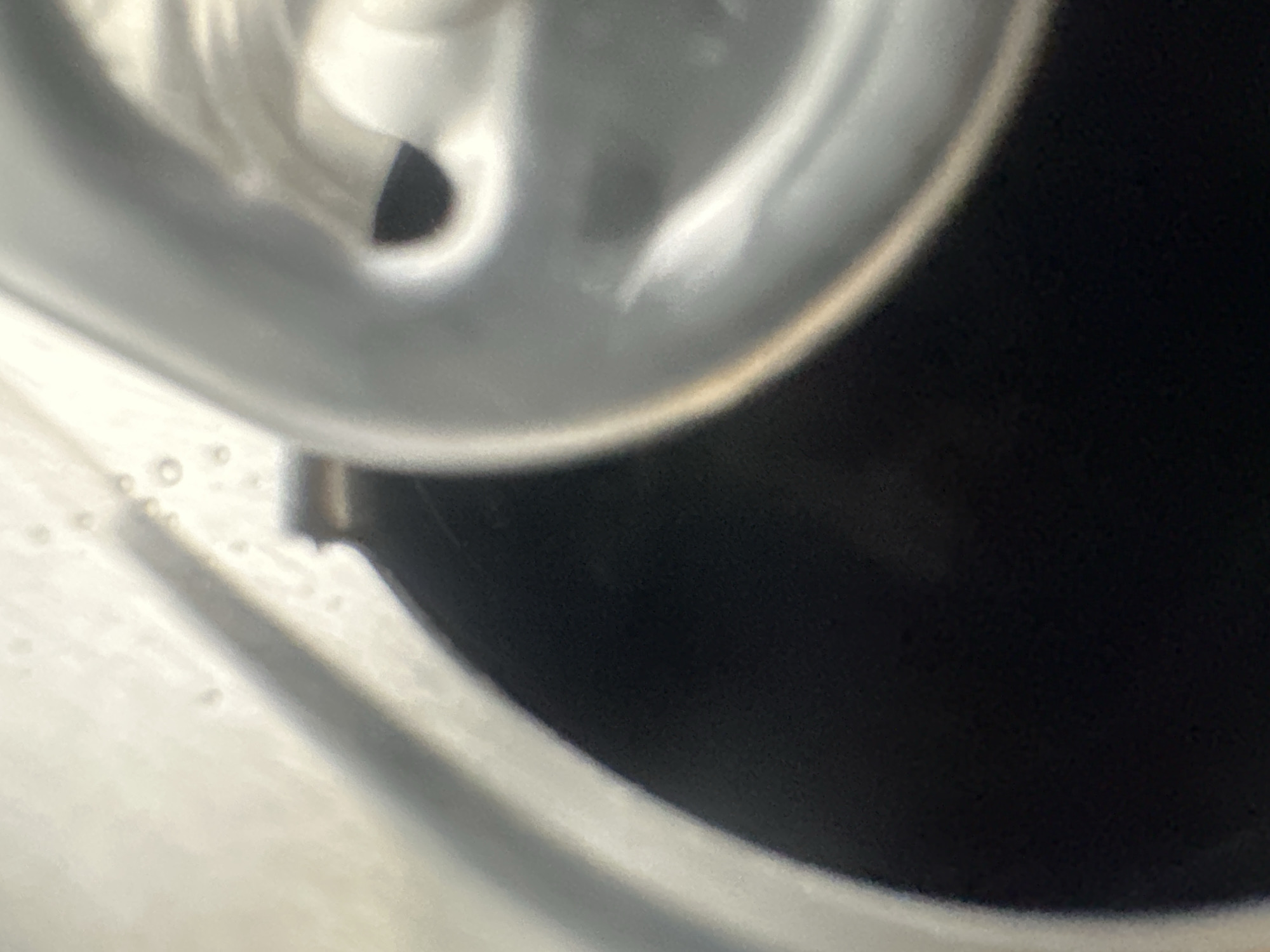 This media file is an extreme close-up, abstract image of what appears to be the interior of a metallic can, possibly a beverage can. The dominant colors are metallic silver and black, with some subtle warm tones suggesting a golden rim or reflection. The surface is highly reflective, showing distorted light patterns and curves. There are no people or discernible scene.
The lighting appears to be artificial, given the sharp reflections and the controlled environment suggested by the metallic material. There are no cues about the time of day or weather. The location context of Belgrade, Serbia, is not visually represented in the image.
Notable details include a small, dark, circular or oval void within the silver surface, which could be an opening or a shadow. There are also small, circular, bubble-like inclusions or textures on the lighter metallic surface in the lower left quadrant of the image. A diagonal shadow or a raised edge cuts across the lower portion of the frame, leading towards the dark area. The overall impression is one of industrial or manufactured material, seen from a very intimate, macro perspective.
There is no visible text in the image. The abstract nature of the close-up makes it difficult to determine the exact object or its purpose, but the metallic sheen and form are characteristic of many types of containers.
