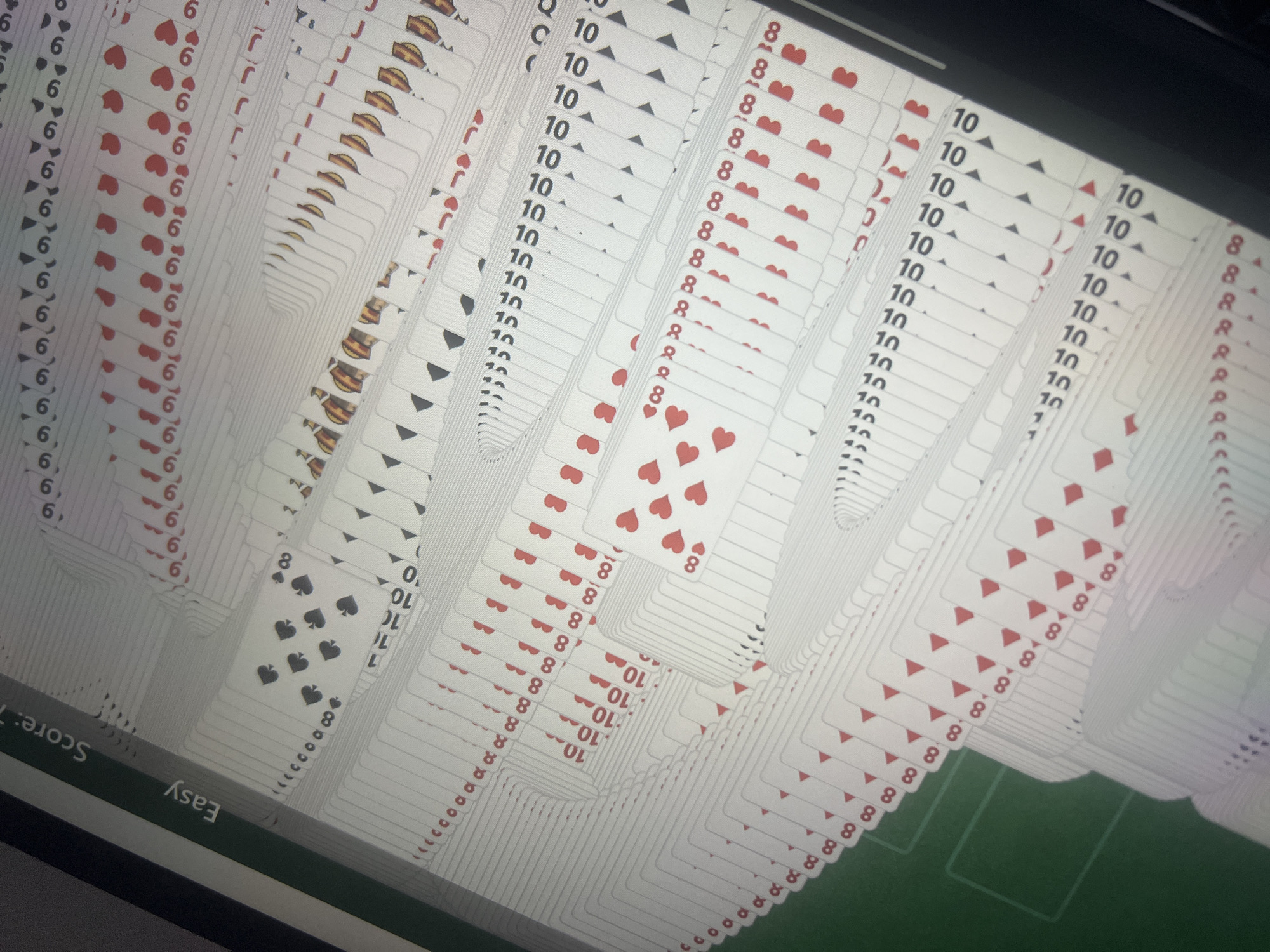 The image shows a computer screen displaying a game of Klondike Solitaire. Multiple columns of playing cards are arranged on a green background. The ranks of visible cards include 6s, Jacks, Queens, 10s, and 8s of various suits. The game appears to be at an advanced stage with many cards dealt. The bottom left corner shows text indicating the game difficulty is set to "Easy" and the score is "7". The image is a close-up shot of the screen, angled slightly. There is no information to identify a location in Dar es-Salaam, Tanzania.