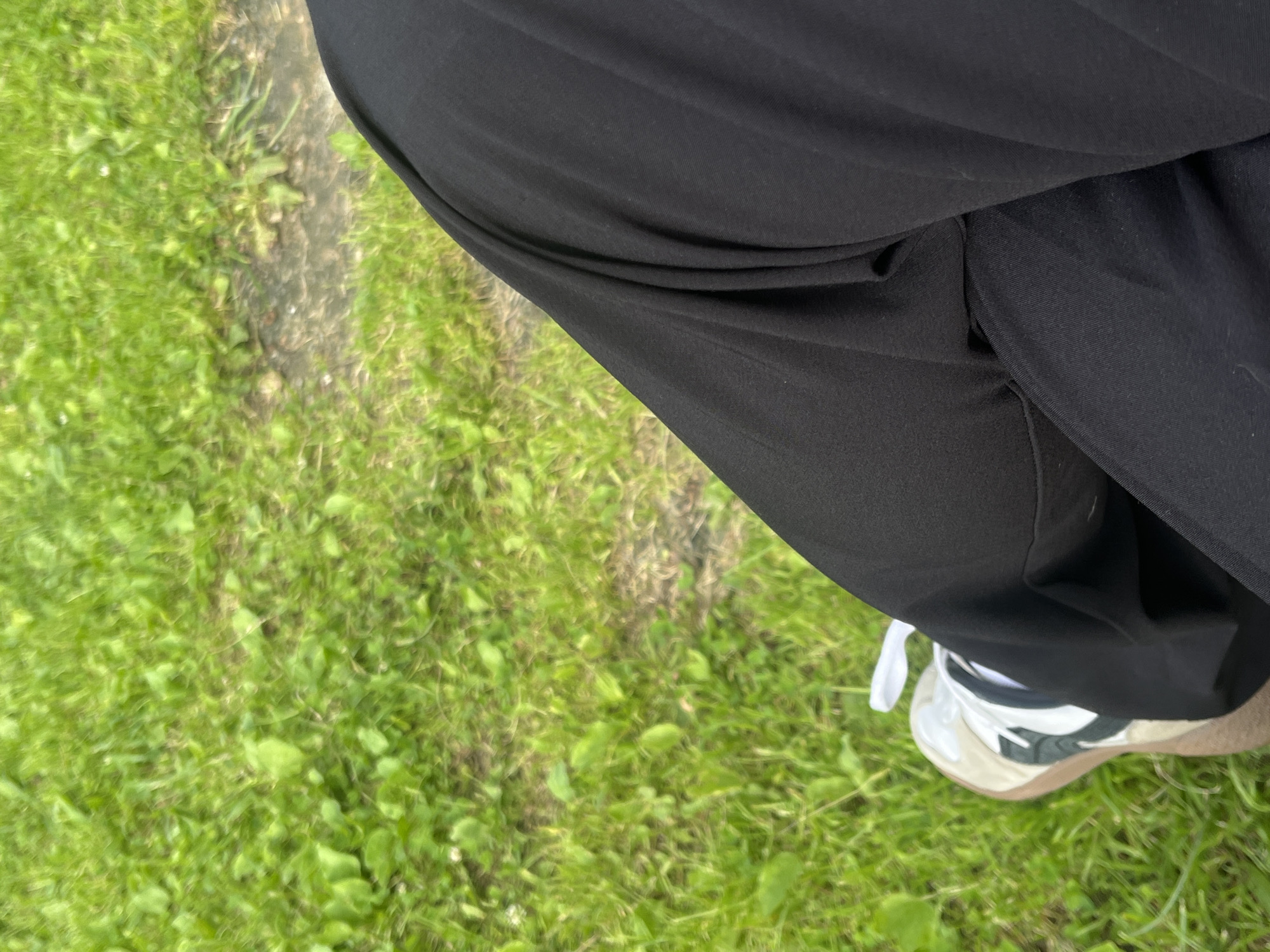 The image is an outdoor shot, showing a person's legs and feet. The person is wearing black pants and a white, tan, and green sneaker. The background is a grassy area with some patches of dirt and possibly fallen leaves. The image is taken from a high angle, looking down at the person's legs and the ground. There is no information available about the specific location in Chelyabinsk, Russia, or the context of the scene.