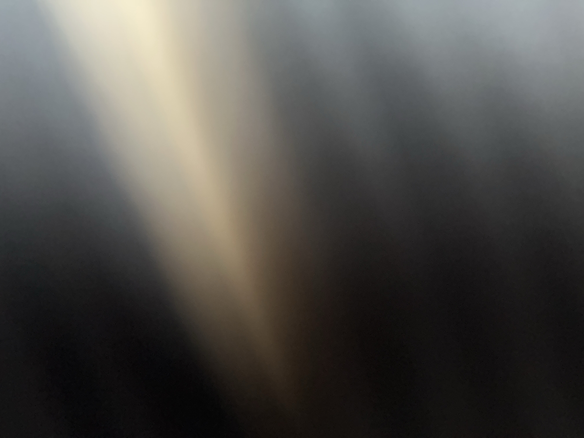The image is an abstract, out-of-focus depiction of light and shadow. A diagonal band of bright, warm light, possibly sunlight or artificial light, enters from the upper right and fades into darker, cooler tones towards the left and bottom. The overall effect is one of diffused light and a sense of depth created by the gradient of colors. There are no discernible objects, people, actions, or interactions visible in the image, nor are there any specific visual cues that would allow for the identification of a location in Belgrade, Serbia. The image is entirely abstract, focusing on the interplay of light and darkness.
