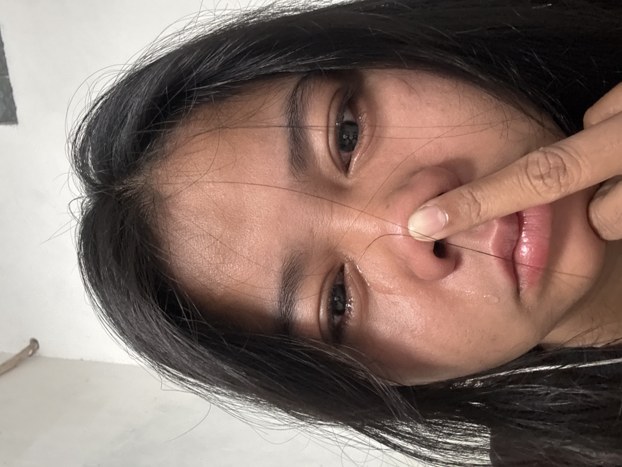 A close-up, slightly angled, portrait-style photograph shows a woman with dark hair and skin. She is touching her nose with her right index finger. Her lips appear glossy, and there is a visible teardrop on her cheek.
The location in the city of North Jakarta, Indonesia, cannot be determined from the visual information.
