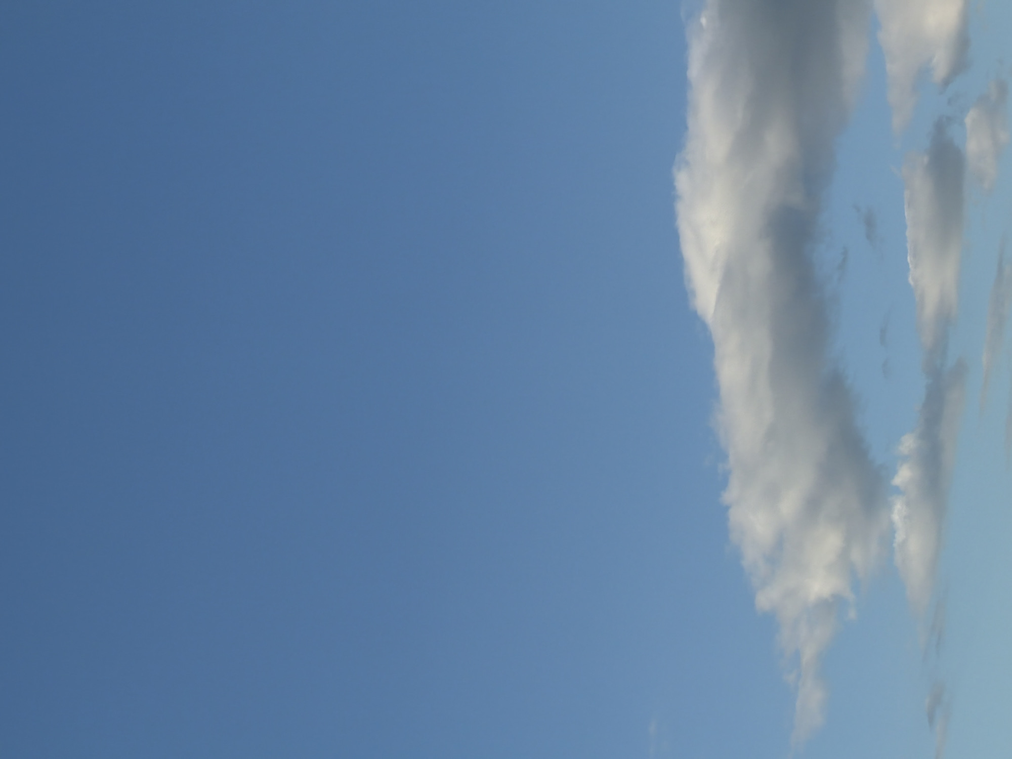 The image shows a clear blue sky with a few scattered clouds. The clouds are white and puffy, and they are located in the lower part of the image. The sky is a light blue color, and it is clear and cloudless in the upper part of the image. The image was taken on a sunny day. There are no people or objects visible in the image. The image depicts an outdoor scene.