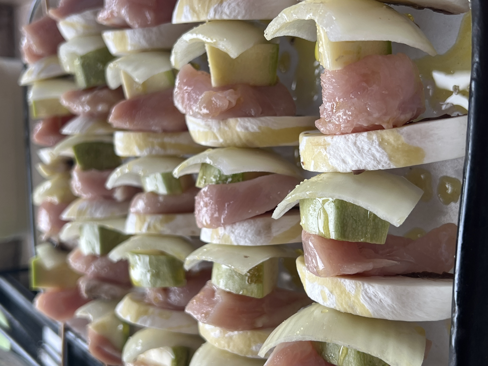 The image shows several skewers filled with alternating pieces of chicken, zucchini and onion. It is unclear if this is in Elena, Bulgaria, as the image provides no location context. The skewers appear to be on a tray, perhaps ready for cooking. Some of the items seem to have been brushed with oil. The presentation suggests they are intended for consumption.