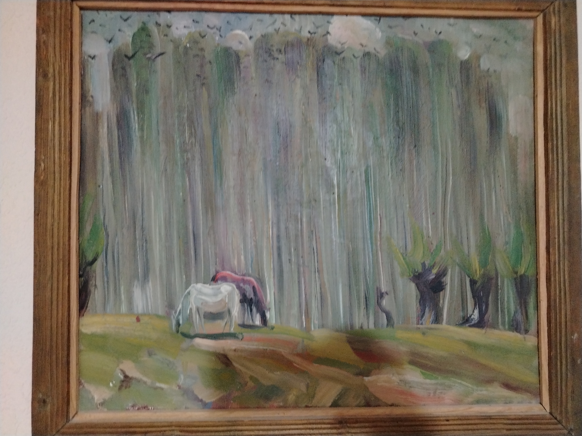 The image is an oil painting framed in wood. The painting depicts a pastoral scene with trees, grass, and two horses in the foreground. One horse is white, and the other is reddish-brown. The trees are tall and slender, creating a dense forest in the background. Birds are visible in the sky. The overall style is impressionistic, with visible brushstrokes and a soft, diffused light. The painting is displayed indoors, against a plain white wall. The location of this artwork in Nukus, Uzbekistan is unknown.