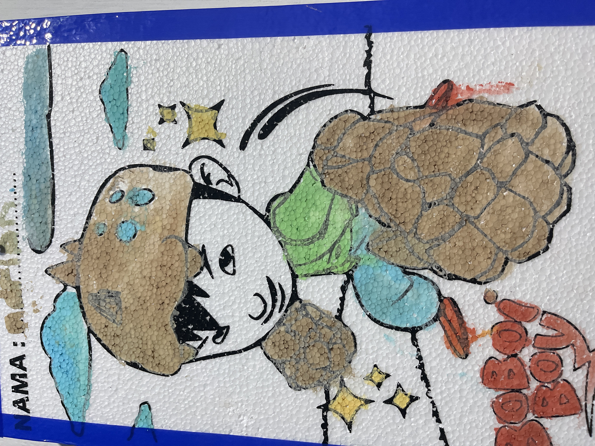 The image displays a colorful drawing on a textured white surface, possibly a piece of styrofoam. The drawing features a cartoon character, likely from the animated series "BoBoiBoy," with brown hair and a green shirt. The character has a determined expression and is depicted in a dynamic pose, with its fists clenched. The drawing incorporates various elements such as blue clouds, yellow stars, and the "BoBoiBoy" logo rendered in red. The use of textured materials for the character's hair, fists, and the background suggests a mixed-media art project. The artwork is bordered by a vibrant blue strip on the right side, suggesting it is part of a larger presentation or object. The overall aesthetic is childlike and energetic. There is no indication of the city of Beuringen, Indonesia, or any specific location within it.