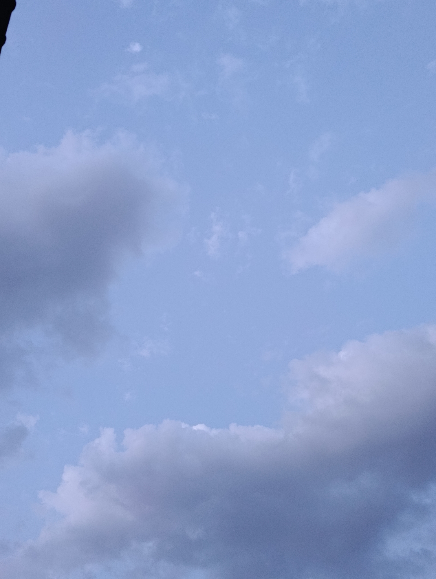 The image shows a cloudy sky with light blue hues. There are no people, subjects, or objects visible in the frame. The environment is an outdoor scene, specifically a sky over the city of Manghit, Uzbekistan.