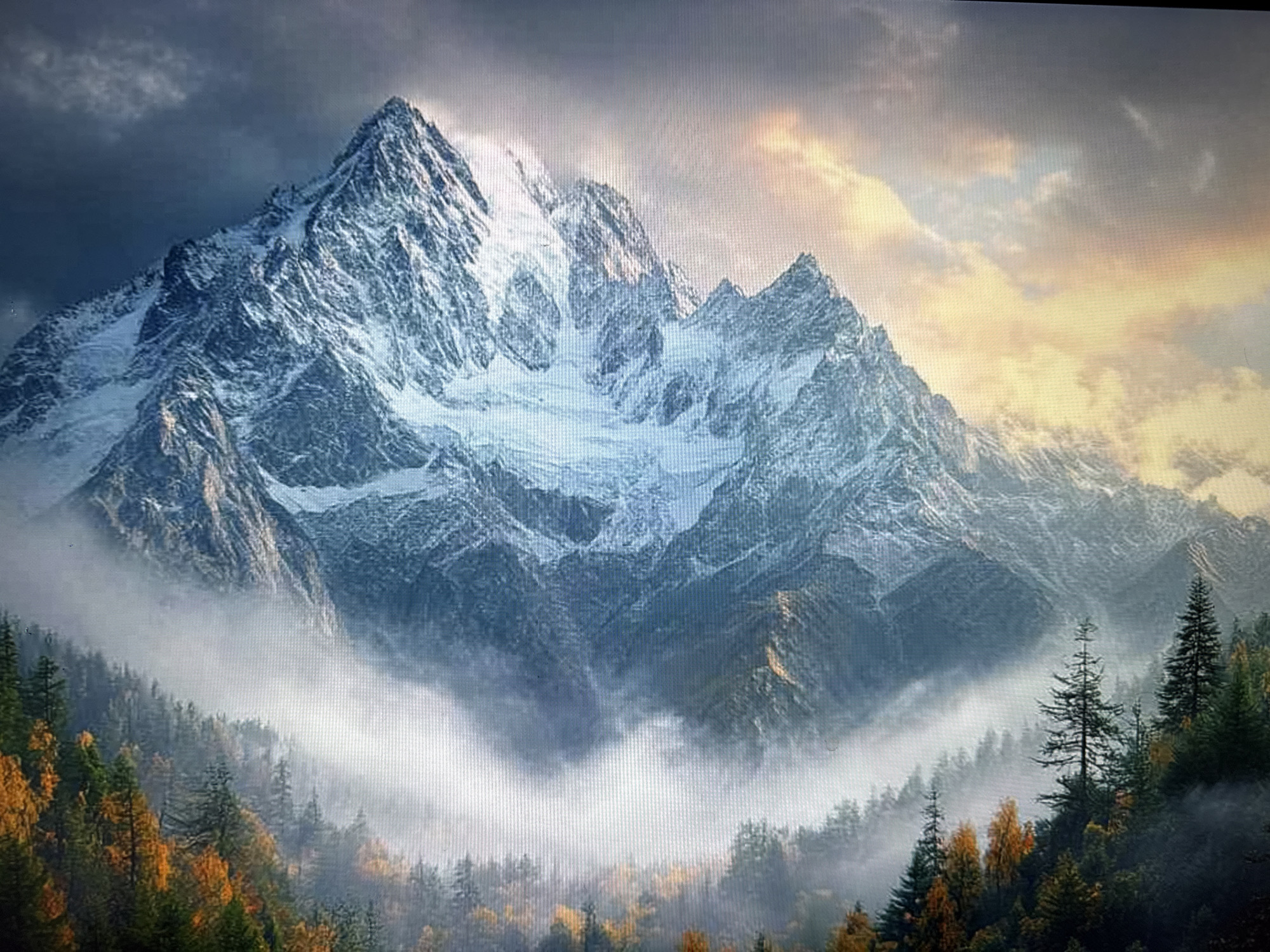 A dramatic and expansive landscape depicts a majestic snow-capped mountain range under a dynamic sky. The central feature is a prominent, jagged peak covered in white snow and ice, flanked by other rugged mountain summits. Lower down, the slopes are a mix of rock and scattered snow.
The sky above transitions from dark, dramatic clouds on the left to warm, golden, and orange-hued clouds on the right, suggesting either a sunrise or sunset. This contrast in lighting creates a powerful atmosphere. Below the formidable peaks, a dense forest fills the valleys and lower mountainous terrain. The trees exhibit a rich palette of deep green conifers interspersed with deciduous trees displaying vibrant yellow and orange autumn foliage. A thick layer of white mist or low-lying clouds weaves through the forest, partially obscuring the base of the mountains and adding a sense of depth and mystery to the scene.
No human activity, structures, or visible text are present, emphasizing the raw and untouched beauty of nature. The image conveys a sense of grandeur, awe, and tranquility within a rugged, possibly cold, mountainous environment.