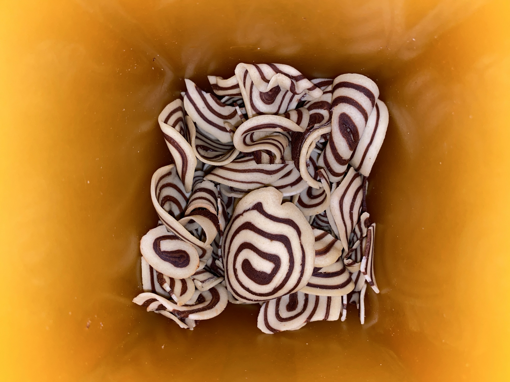 The image shows a top-down view of a collection of curled cookies with a striped pattern of dark brown and white. The cookies are contained within a yellow or light brown container. There are no people visible in the image, and no specific location in Lhokseumawe, Indonesia can be determined from the given information. The focus is entirely on the arrangement of the cookies within the container.