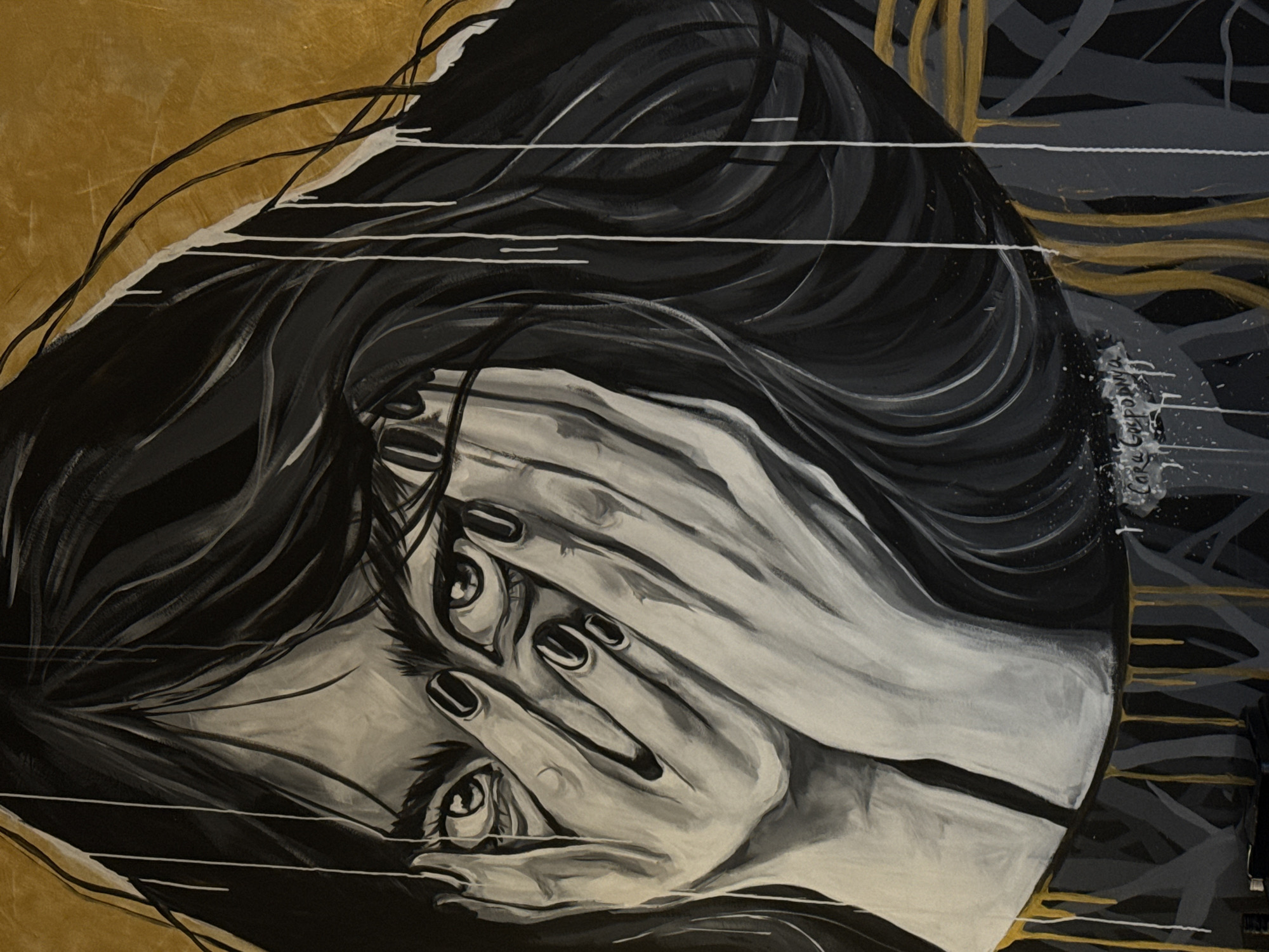 A rotated medium-angle shot of an art piece depicting a woman covering her face with her hands. The woman's face is partially obscured, but her eyes are visible peering out from behind her hands. Her hair is long, flowing, and dark, contrasting with her pale skin. The painting is rendered in shades of black, gray, white, and gold, with visible brushstrokes adding texture. The background features abstract elements, including drips and splatters, in similar colors. A handwritten signature can be discerned. The location is not explicitly mentioned or visibly depicted in the image. Therefore, the city of Krasnoyarsk, Russia, cannot be confirmed as the location.