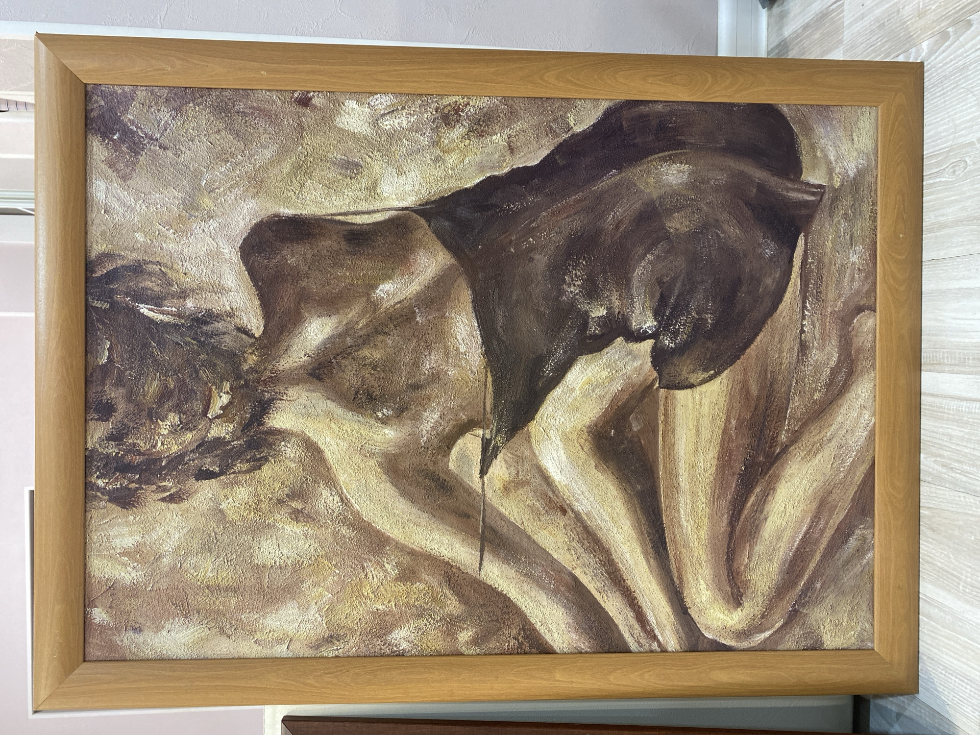 A framed oil painting depicts a person embracing their knees in a fetal position, rendered in shades of brown and tan. The painting is mounted on a wall, likely indoors, in Unknown, Unknown.