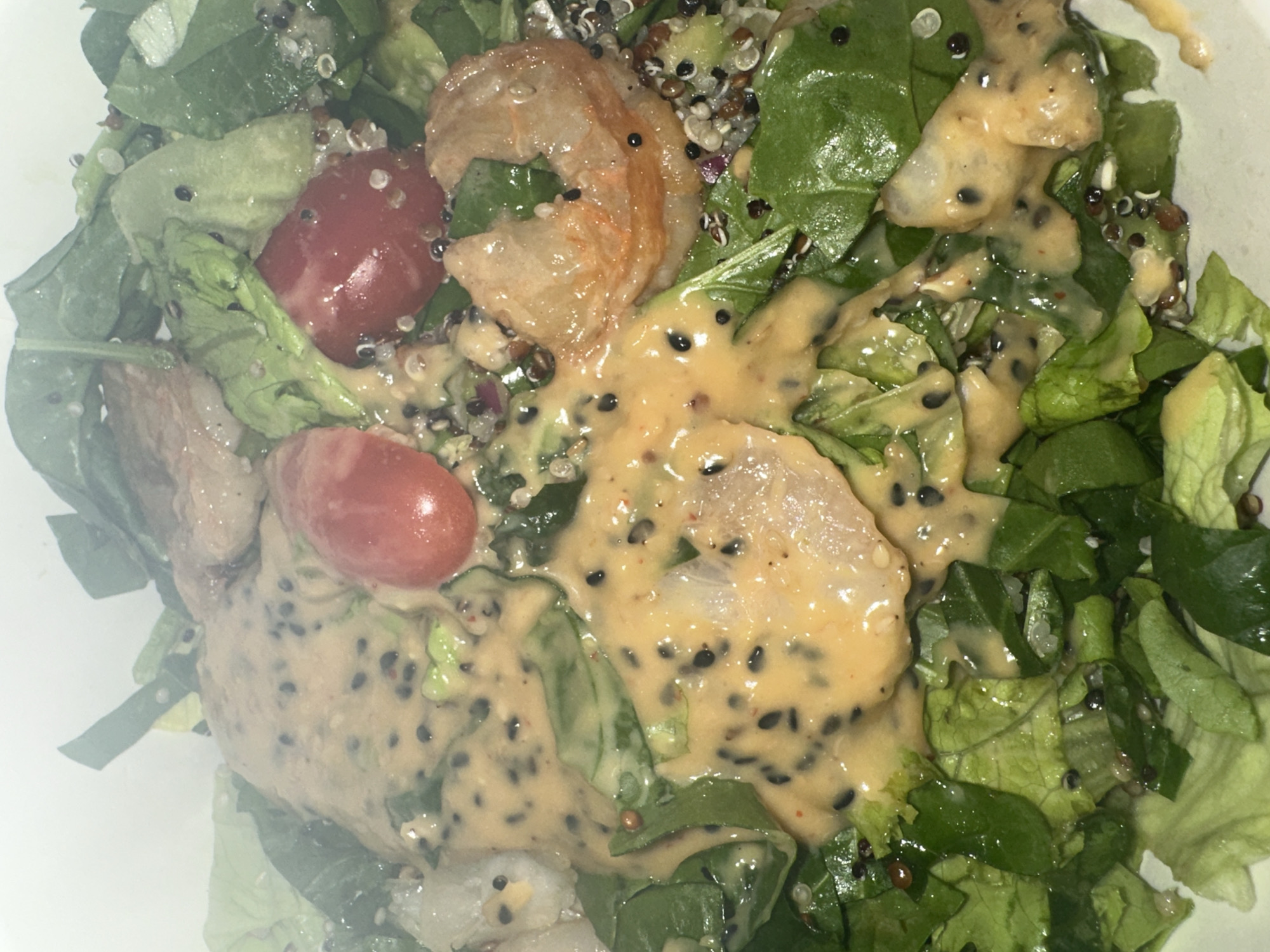 The image depicts a salad consisting of lettuce, spinach, quinoa, cherry tomatoes, and shrimp, dressed with a creamy, sesame seed dressing. The specific location within the city of Sofia, Bulgaria cannot be determined from the image. There are no people visible in the image.