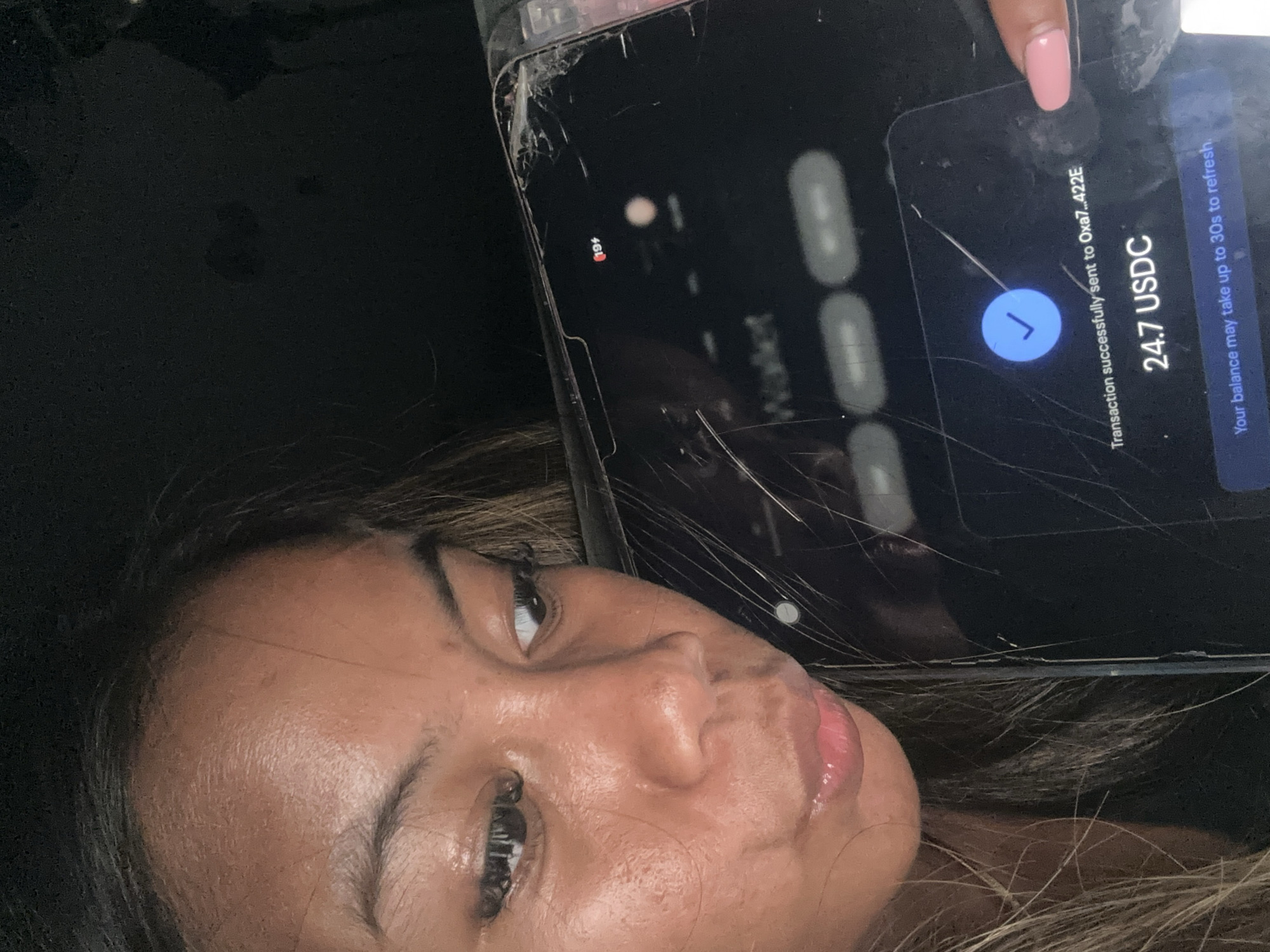 A woman is taking a selfie showing the screen of a cracked phone. The phone screen shows a successful transaction of 24.7 USDC to an address beginning with "Oxa7...422E". The phone displays 194 unread notifications. The location of North Jakarta, Indonesia, cannot be determined from the image.