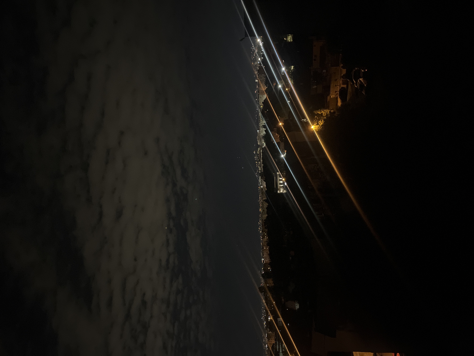 The image depicts a nighttime view of a city skyline. The left side of the frame features a cloudy sky, illuminated by distant city lights. The right side shows a city landscape at night, with buildings and streetlights creating streaks of light. The location is identified as Sofia, Bulgaria.