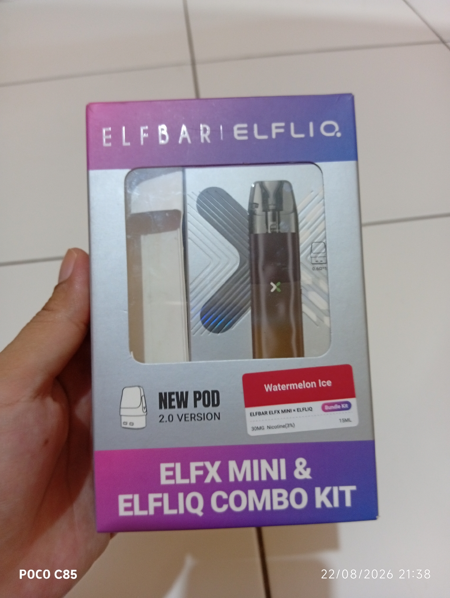 The image shows a close-up of a product box for "ELFX MINI & ELFLIQ COMBO KIT" with a "Watermelon Ice" flavor. The box has a gradient of pink and purple. Inside the clear plastic packaging, a vape device is visible. The bottom left corner of the image displays "POCO C85" and the bottom right corner shows "22/08/2026 21:38". The scene appears to be indoors, possibly on a tiled floor, and is likely a product display or personal item. There is no indication of the location being in the city of South Tangerang, Indonesia.
