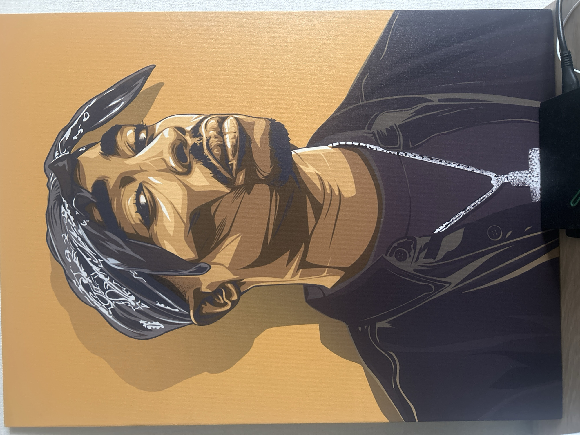 The image is a portrait of Tupac Shakur, depicted on a canvas with a light orange background. He is wearing a black bandana with white designs, a dark purple jacket with two buttons visible, and a white cross necklace. The artwork is rendered in a stylized, graphic manner with defined lines and shading.