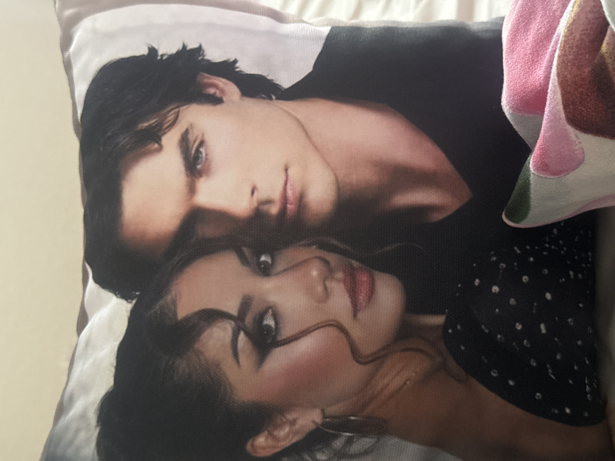 The image shows a rectangular throw pillow featuring a print of two people. The person on top appears to be a male with dark hair, light skin, and blue eyes, wearing a dark-colored shirt or jacket. The person below is a female with dark hair, light skin, and dark eyes, wearing a dark top with small white dots. The pillow is resting on a light-colored surface. The location of the image and the city of Mirkovo, Bulgaria cannot be determined based on the content of the image.